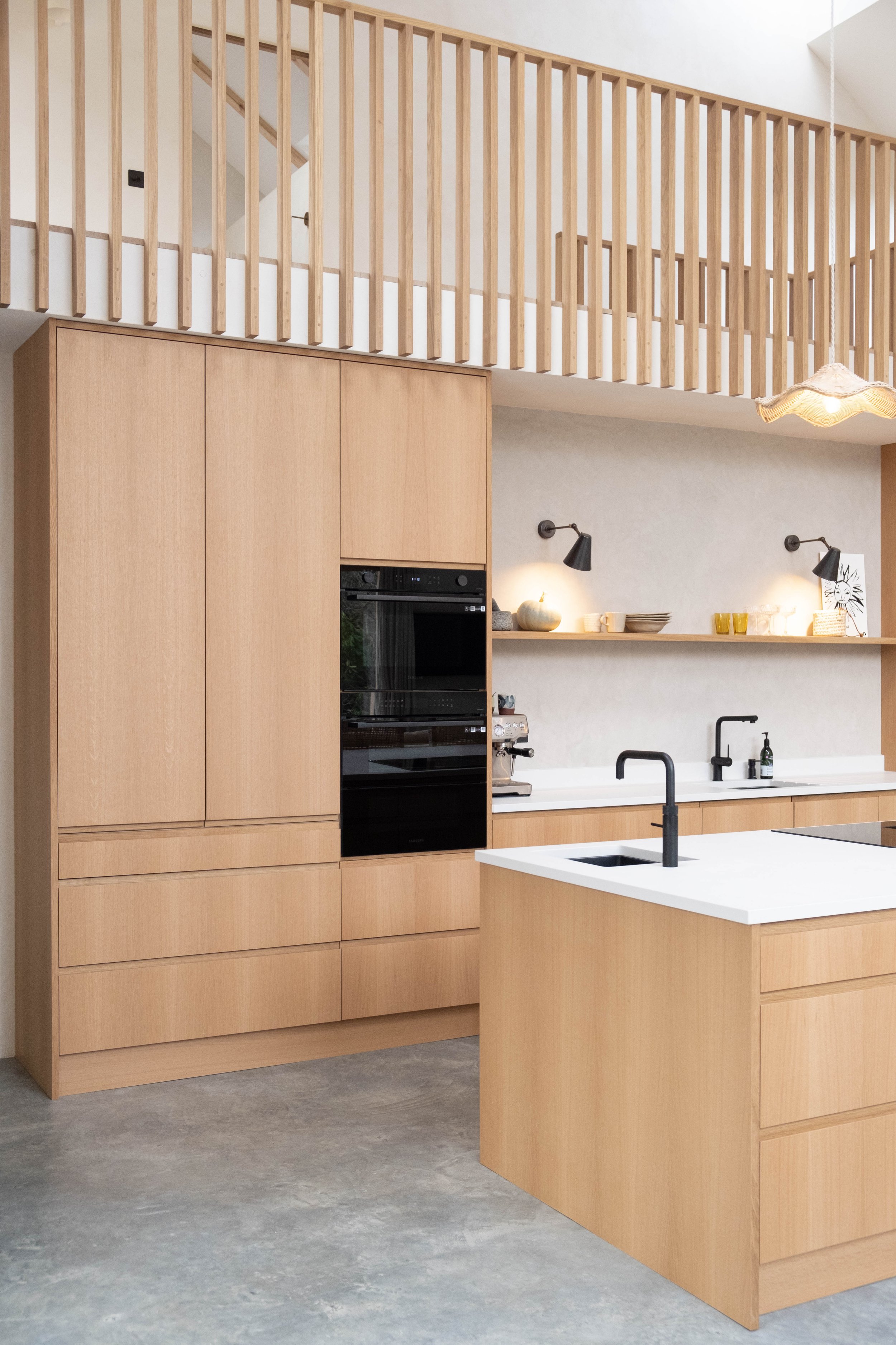 Modern kitchen with light wood cabinets, a kitchen island with a white countertop, black sink, black faucet, and a backsplash shelf with decorative items.