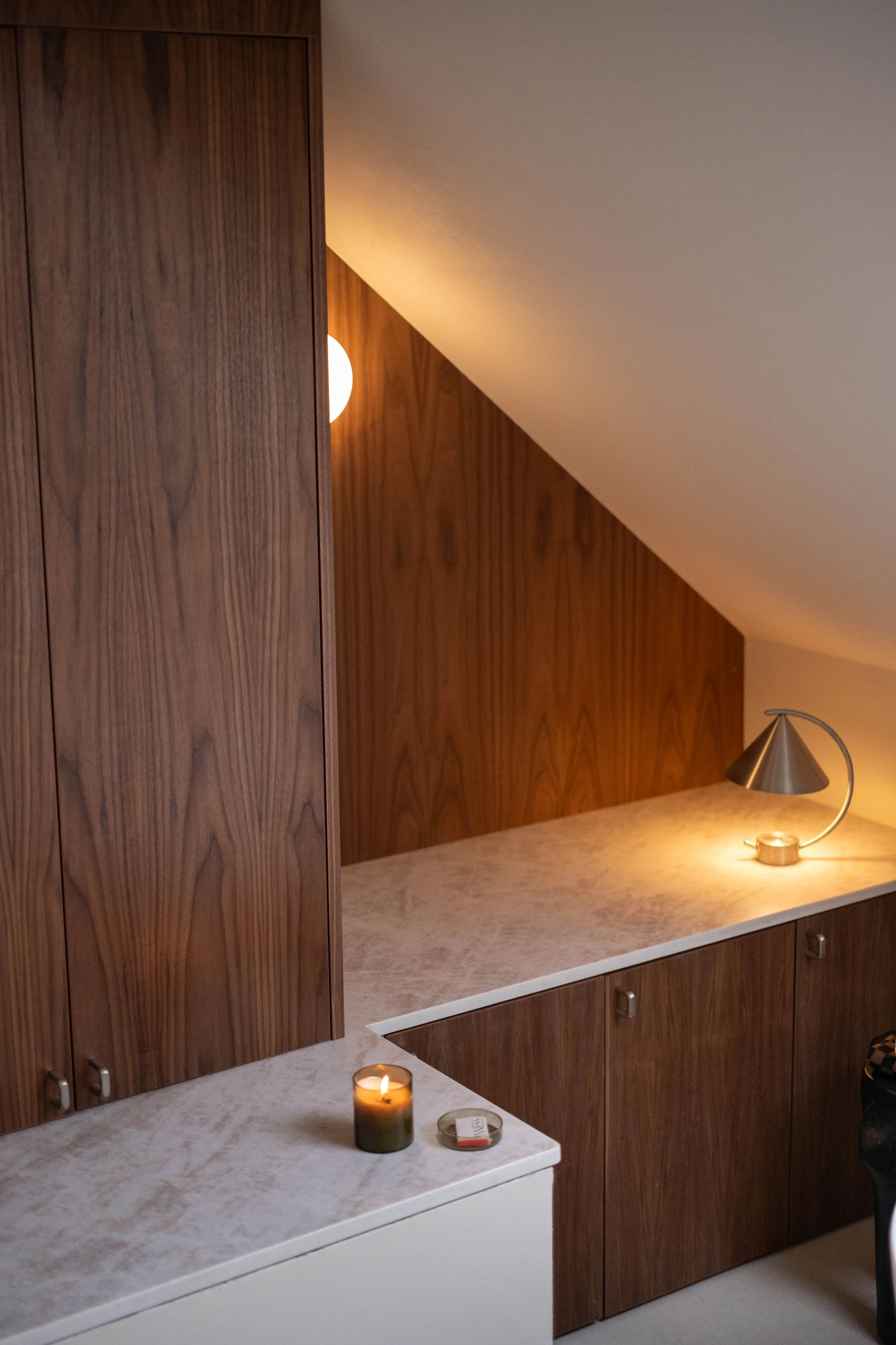 A corner of a kitchen with wooden cabinets and a white marble countertop. On the countertop, there is a lit candle and a small dish.