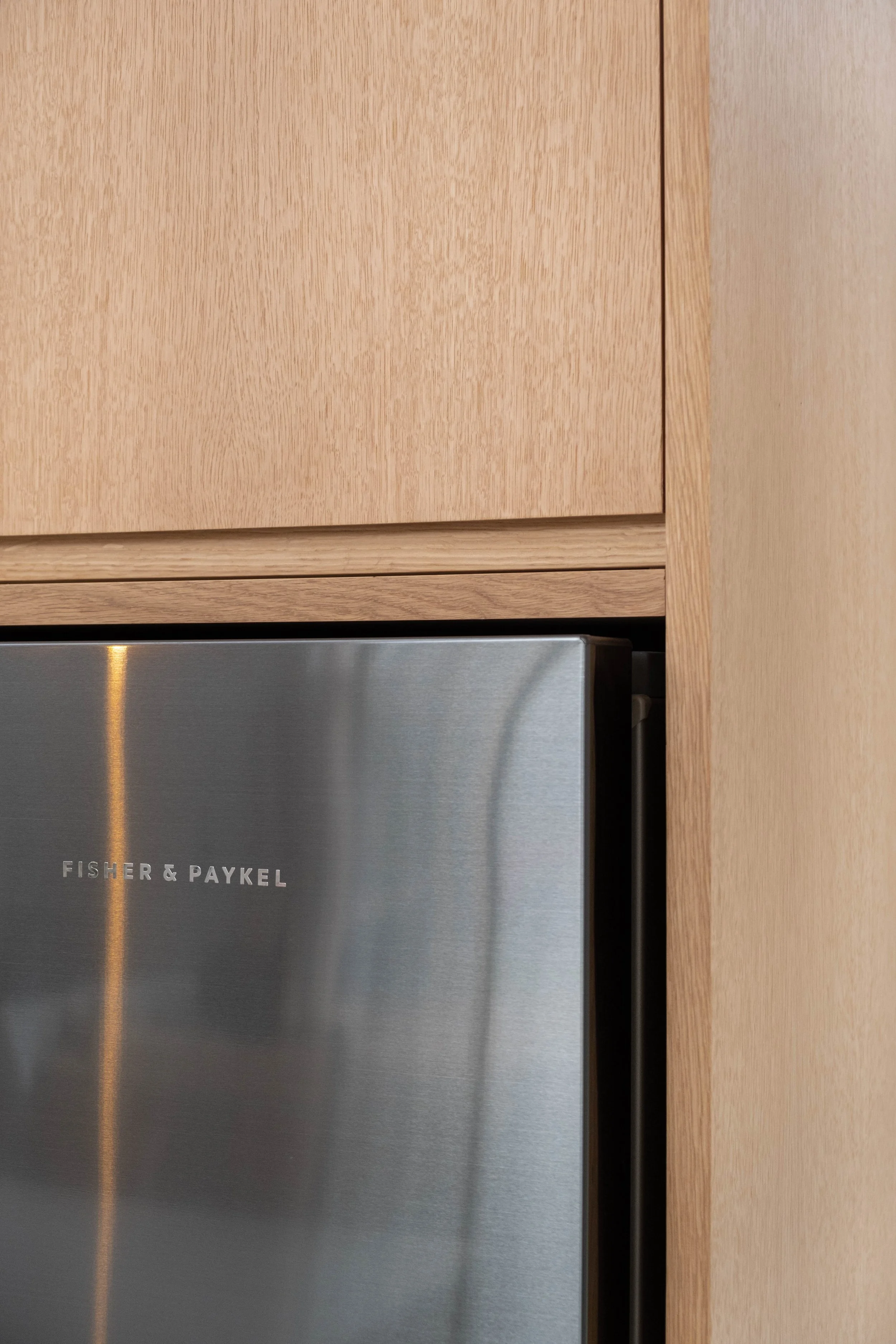 Close-up of a stainless steel Fisher & Paykel refrigerator with a wooden cabinet above it.