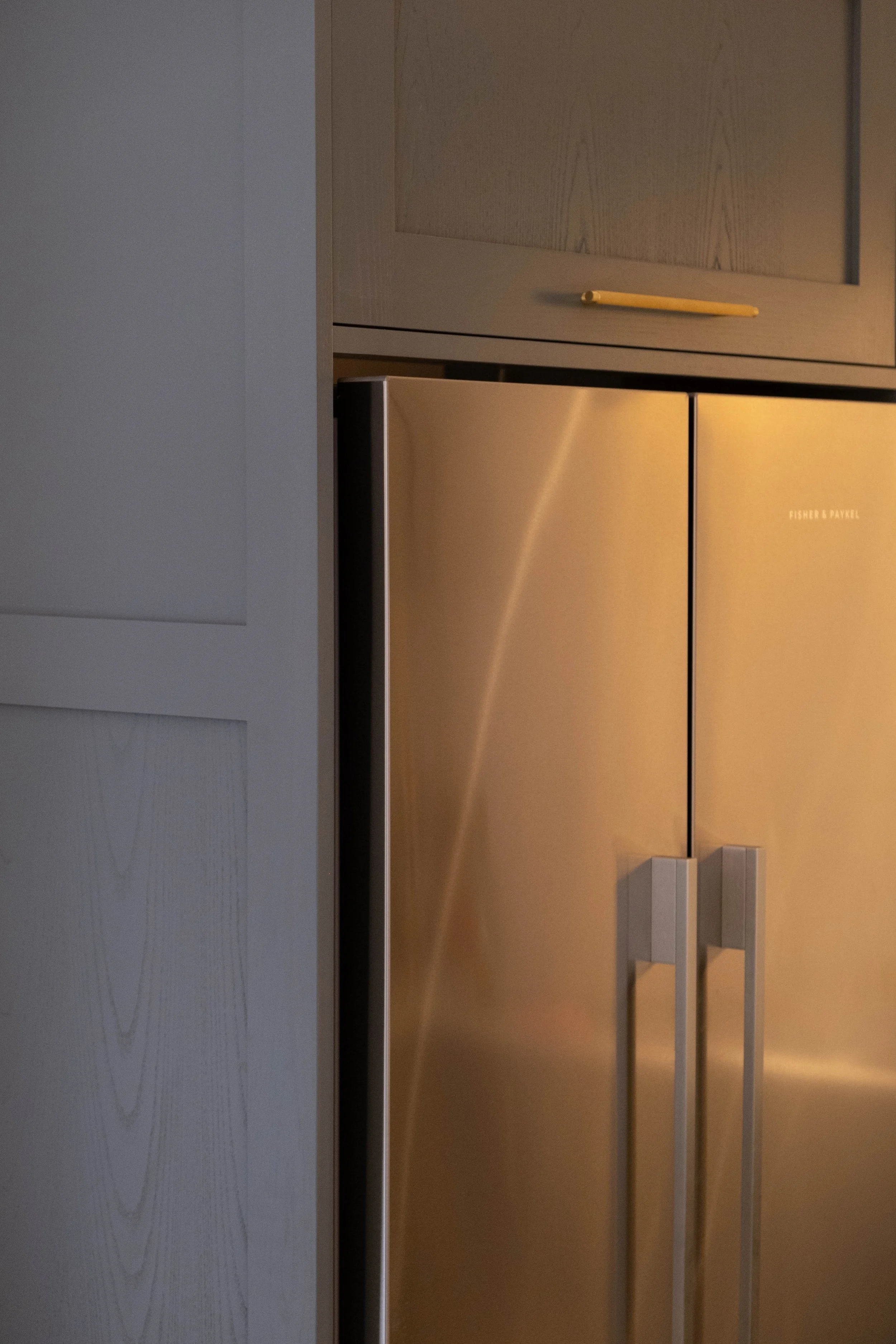 Close-up of a refrigerator door with a wooden cabinet above it in a kitchen.