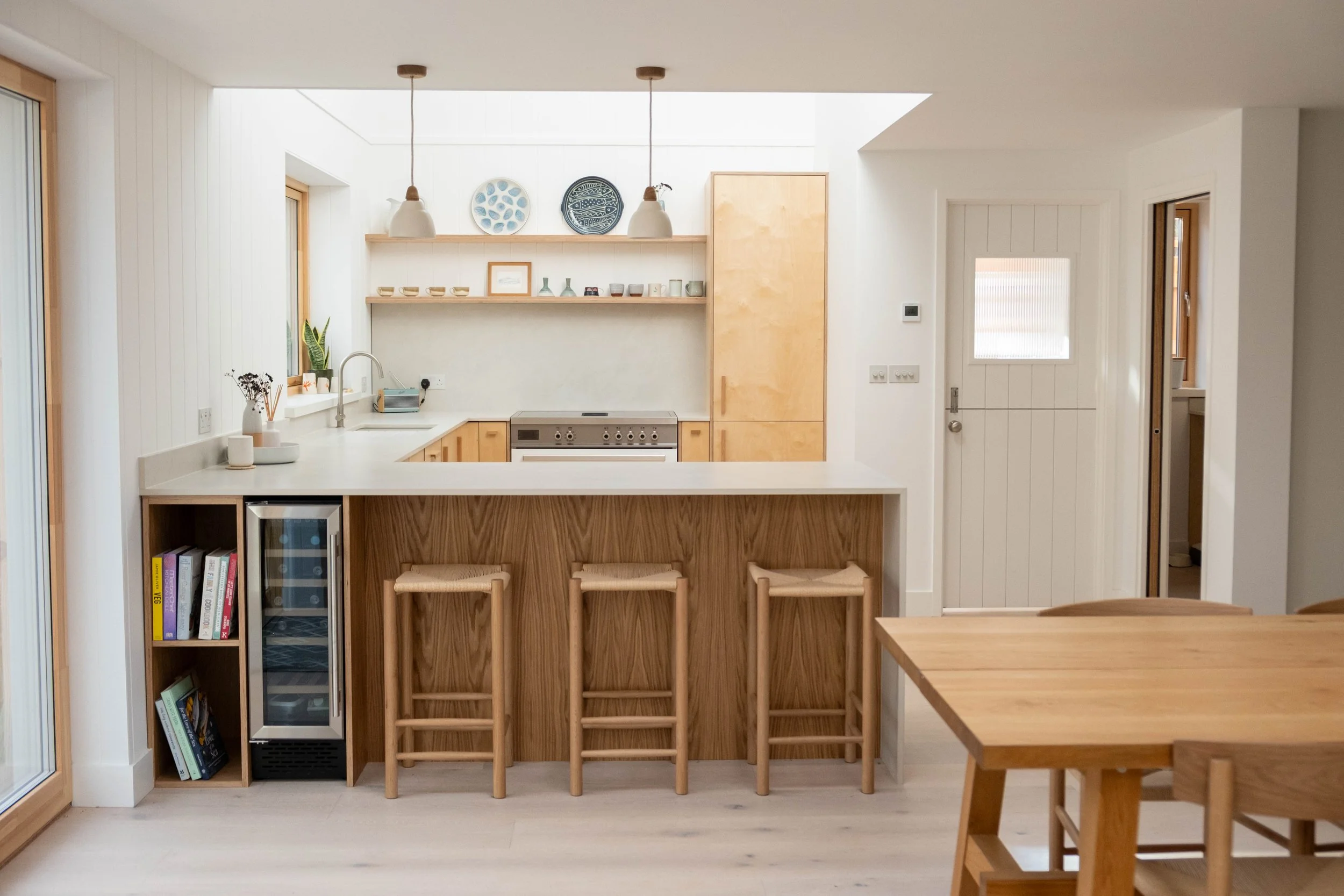 A modern kitchen with a white countertop, wooden cabinets, and a study area with four wooden stools in front.