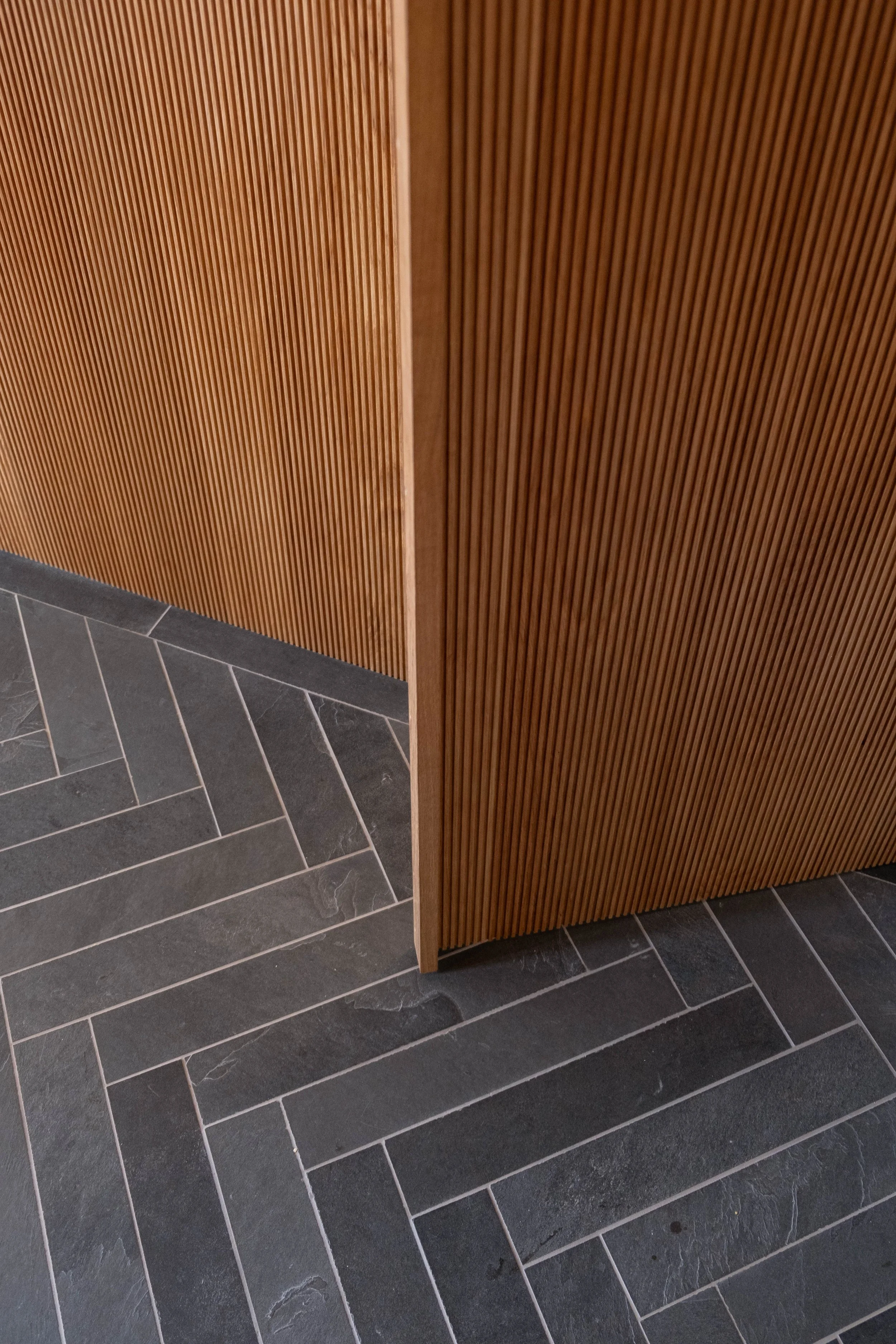 Close-up of a wooden slatted partition with dark gray tiled floor underneath.
