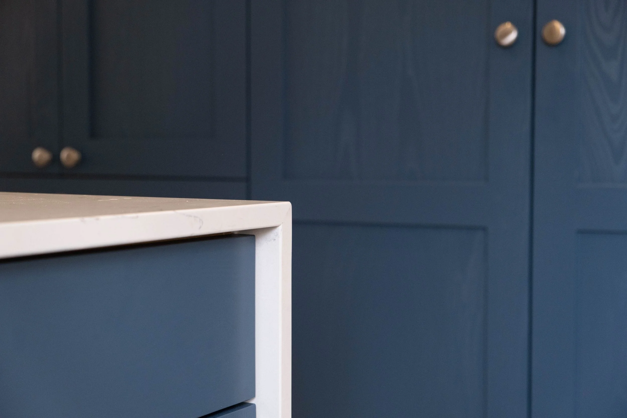 Close-up of a white table or cabinet with a smooth surface, against a background of dark blue cabinets with metal knobs.