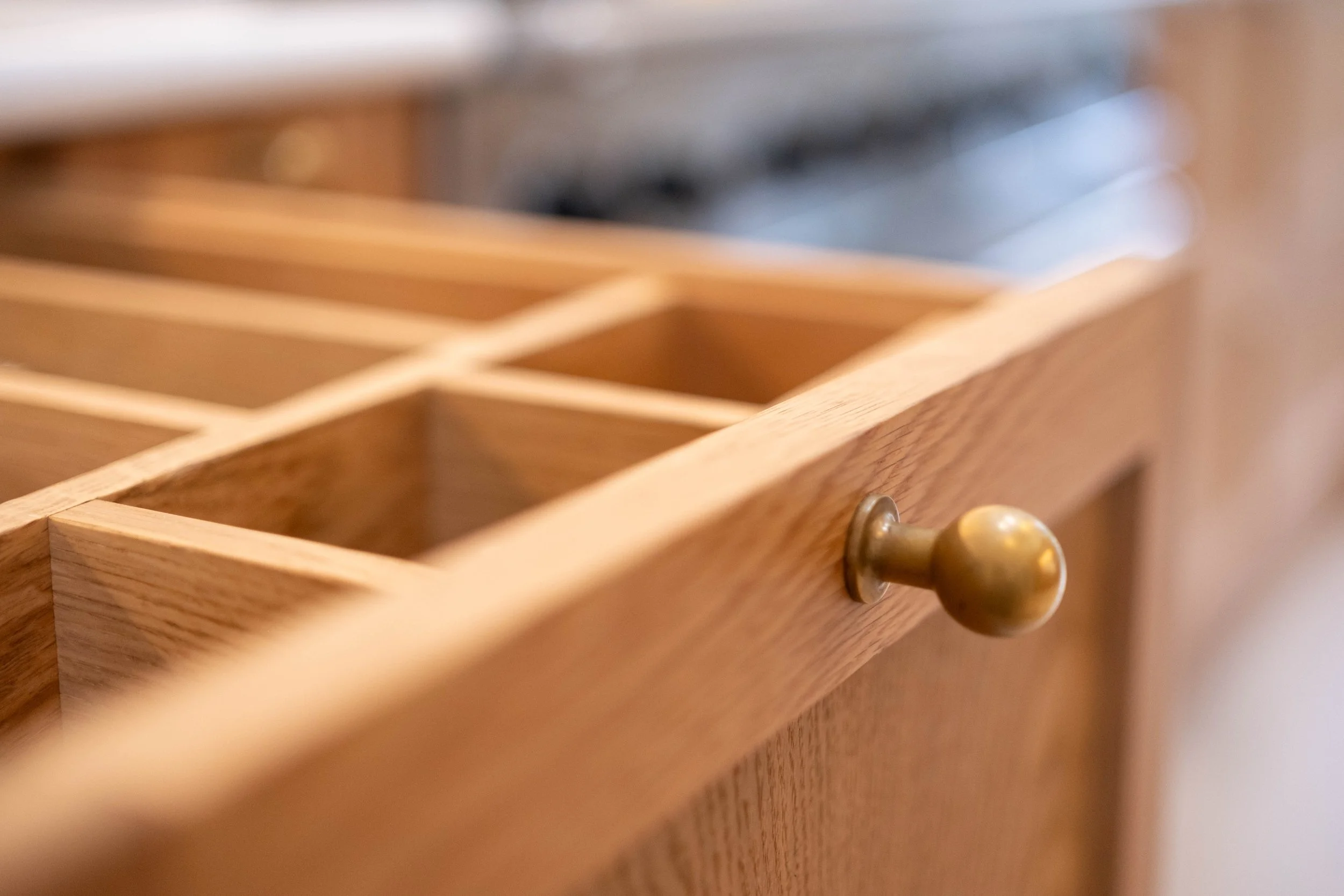 Close-up of an open wooden drawer with a brass knob, showing divided compartments inside.