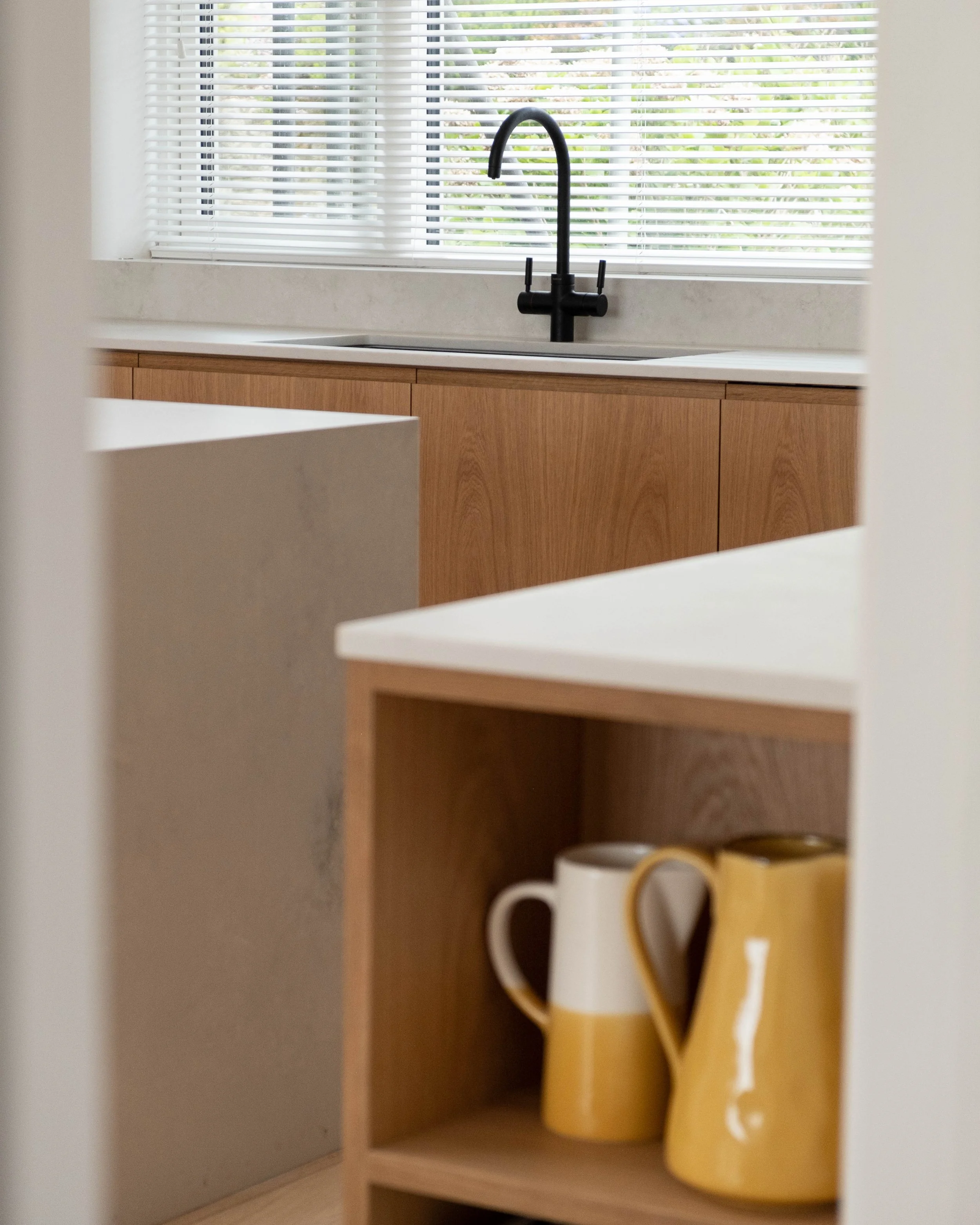 Kitchen with a window with blinds, black sink faucet, wooden cabinets, and a decorative yellow and white wooden 'LOVE' sign.