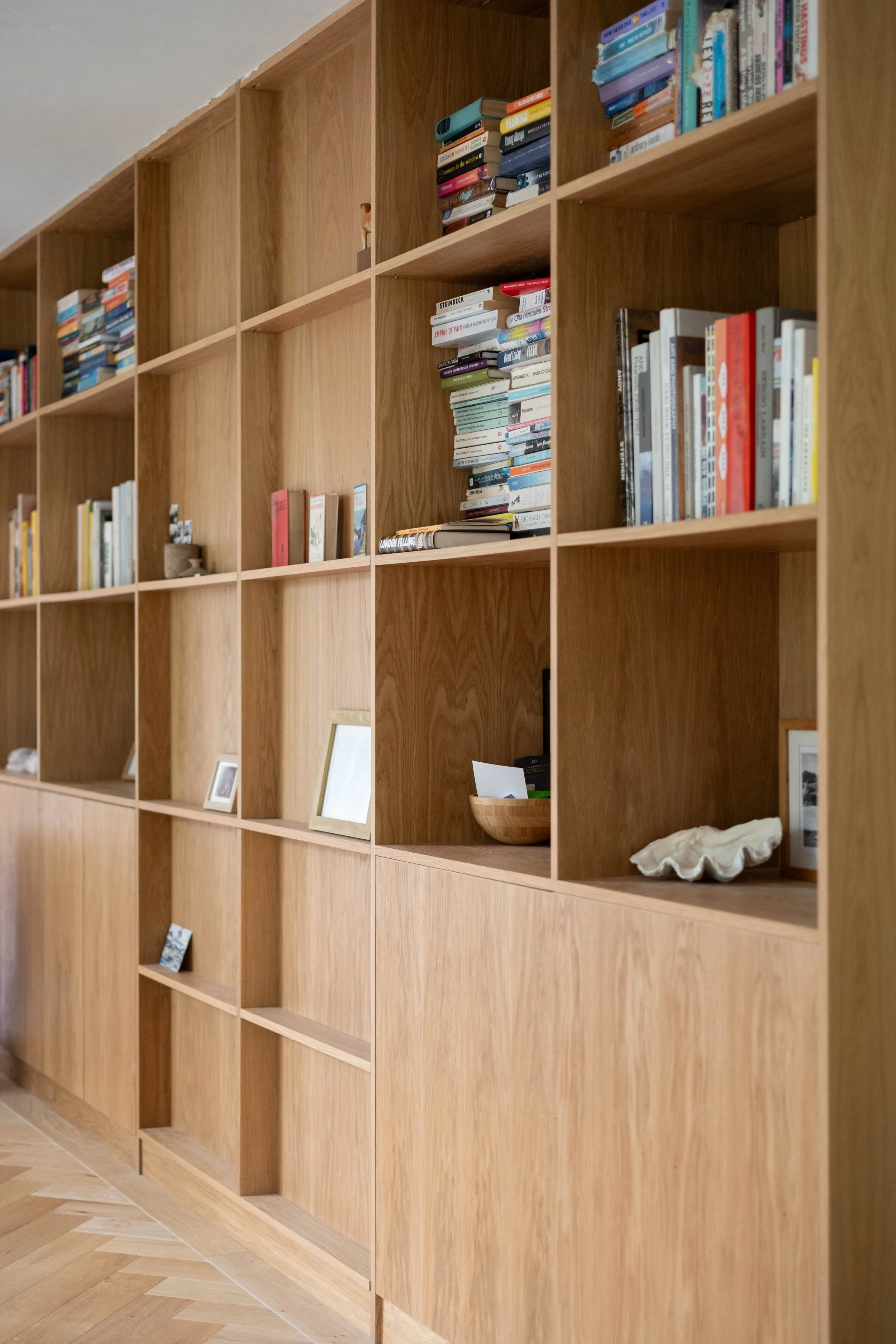 Wooden bookshelf filled with books, picture frames, a bowl, and decorative shells