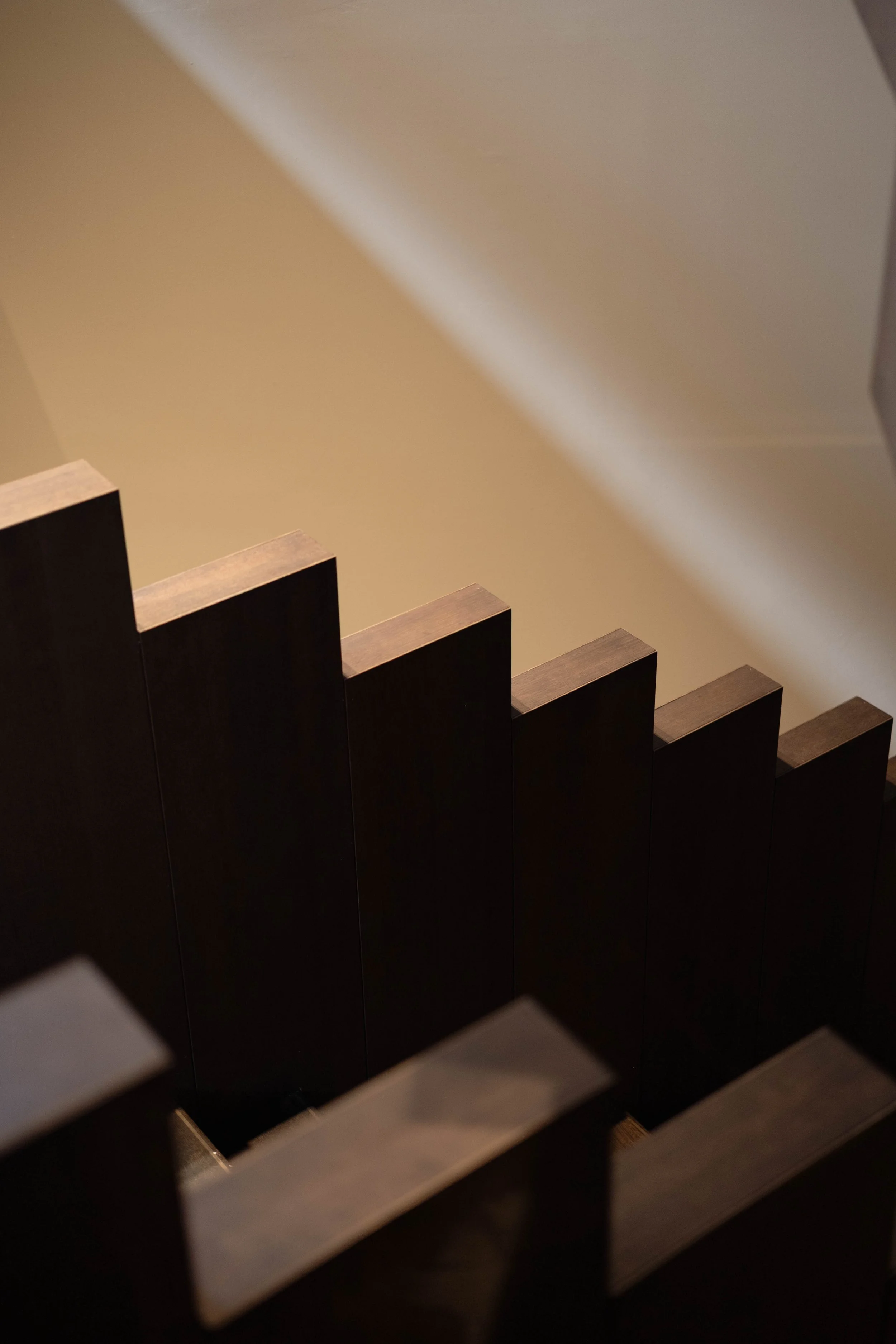 A staircase with dark wooden steps and a beige wall with light shadows.