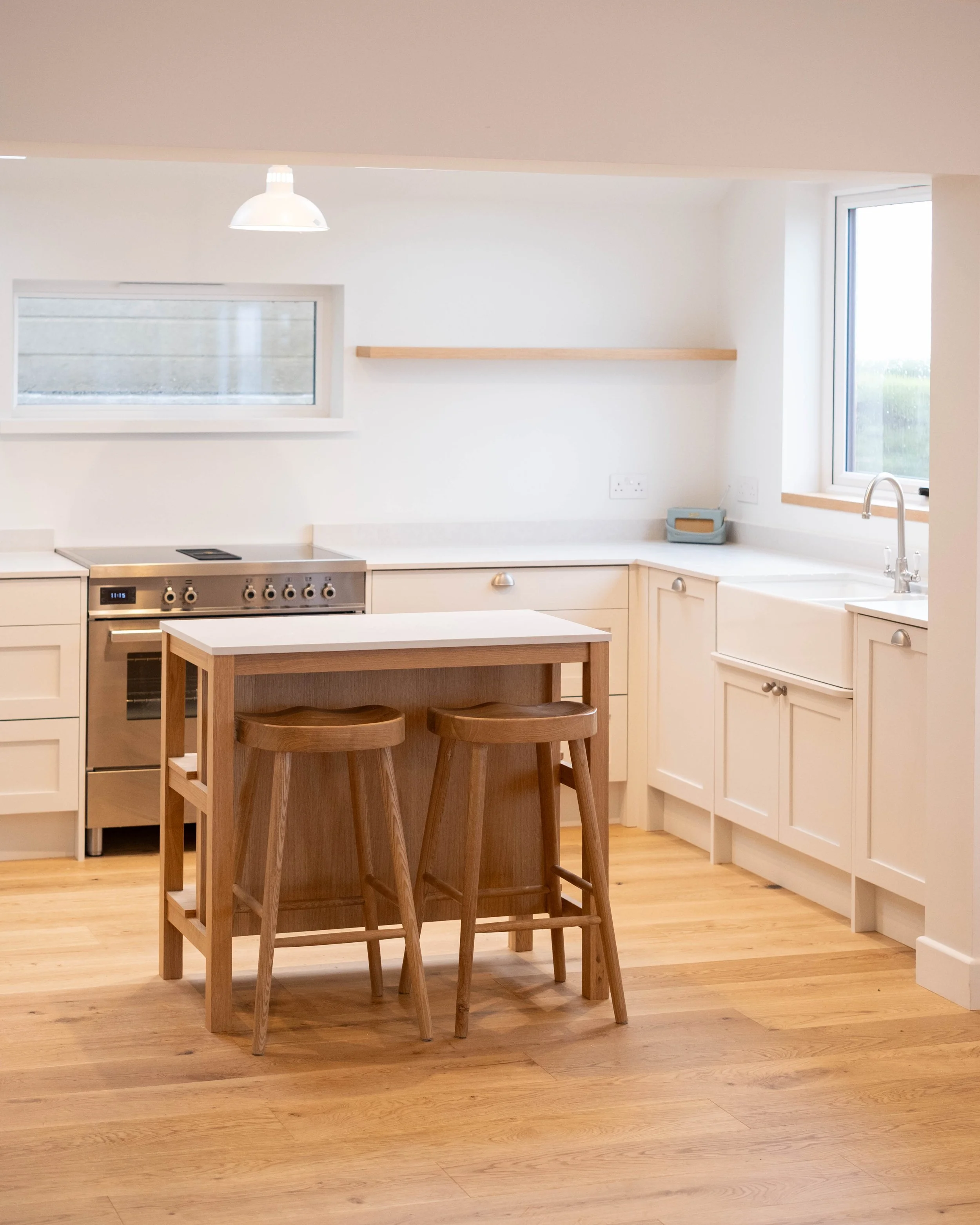 A modern kitchen with white cabinets, a wooden kitchen island with stools, a built-in oven, a window above the sink, and a minimalist decor.
