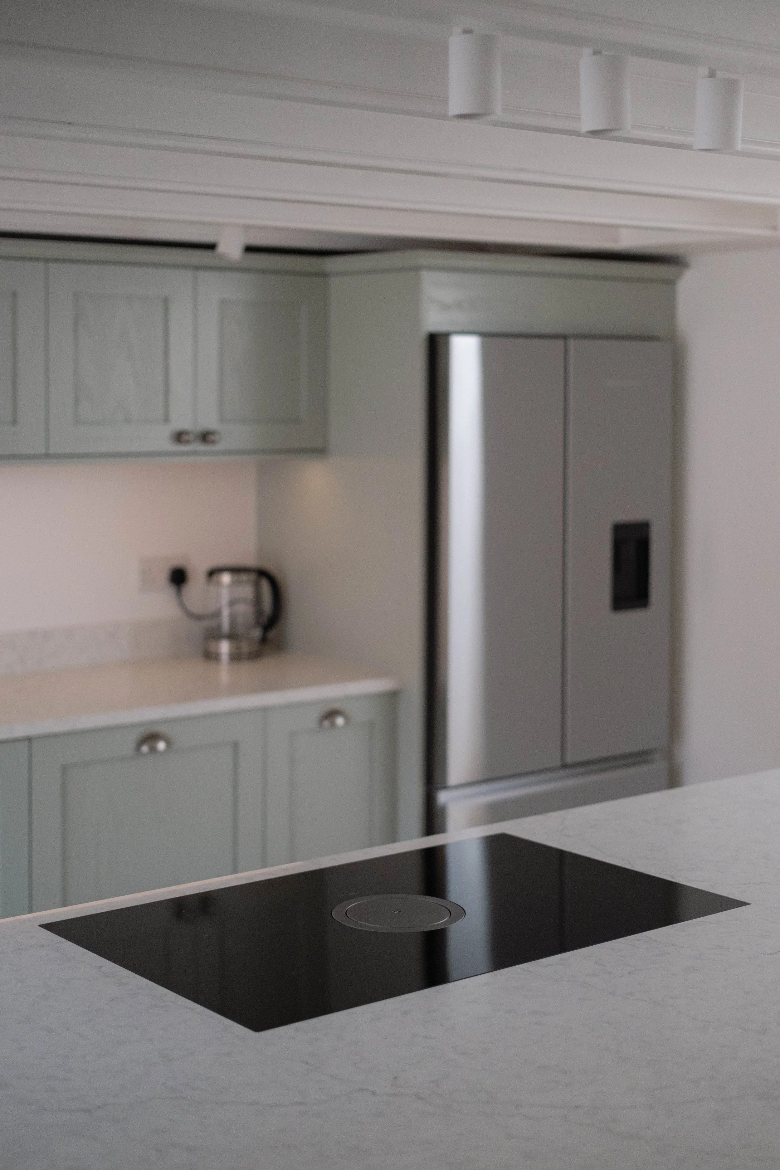 Modern kitchen with gray cabinets, a black induction cooktop on a white countertop, a stainless steel refrigerator, and a coffee maker on the counter.