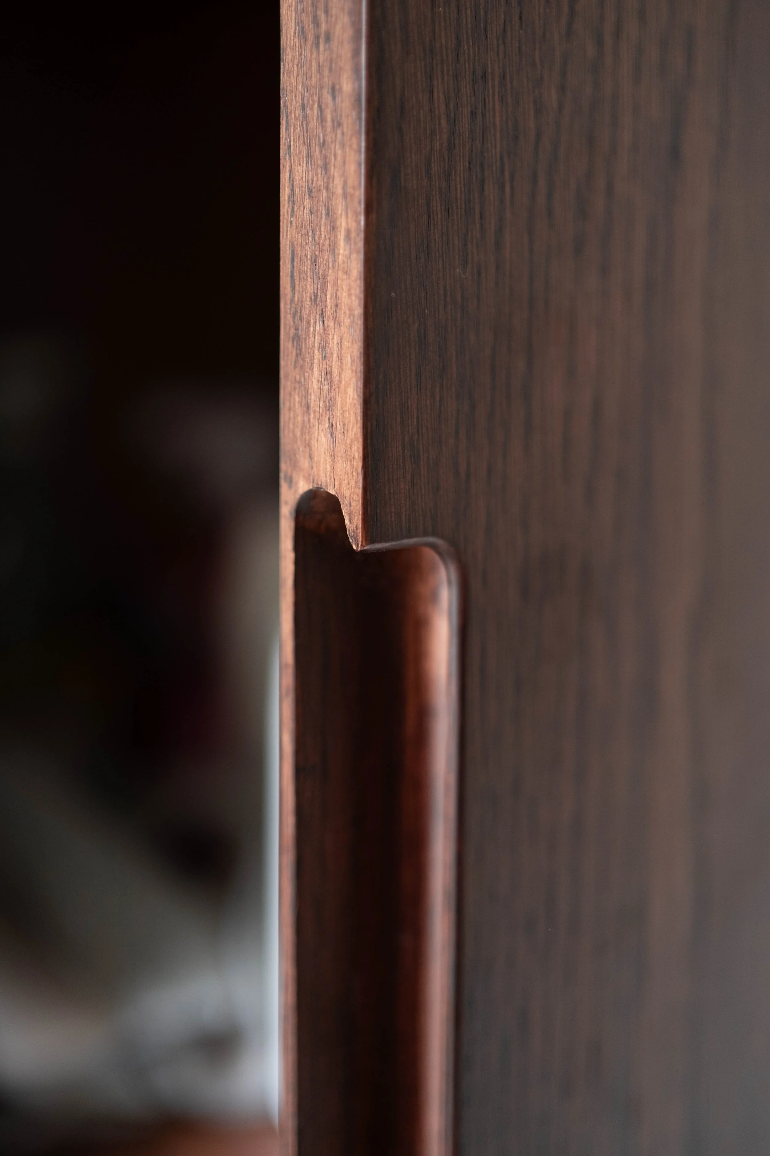 Close-up of a dark wooden furniture piece, focusing on the side and a small cutout at the bottom.
