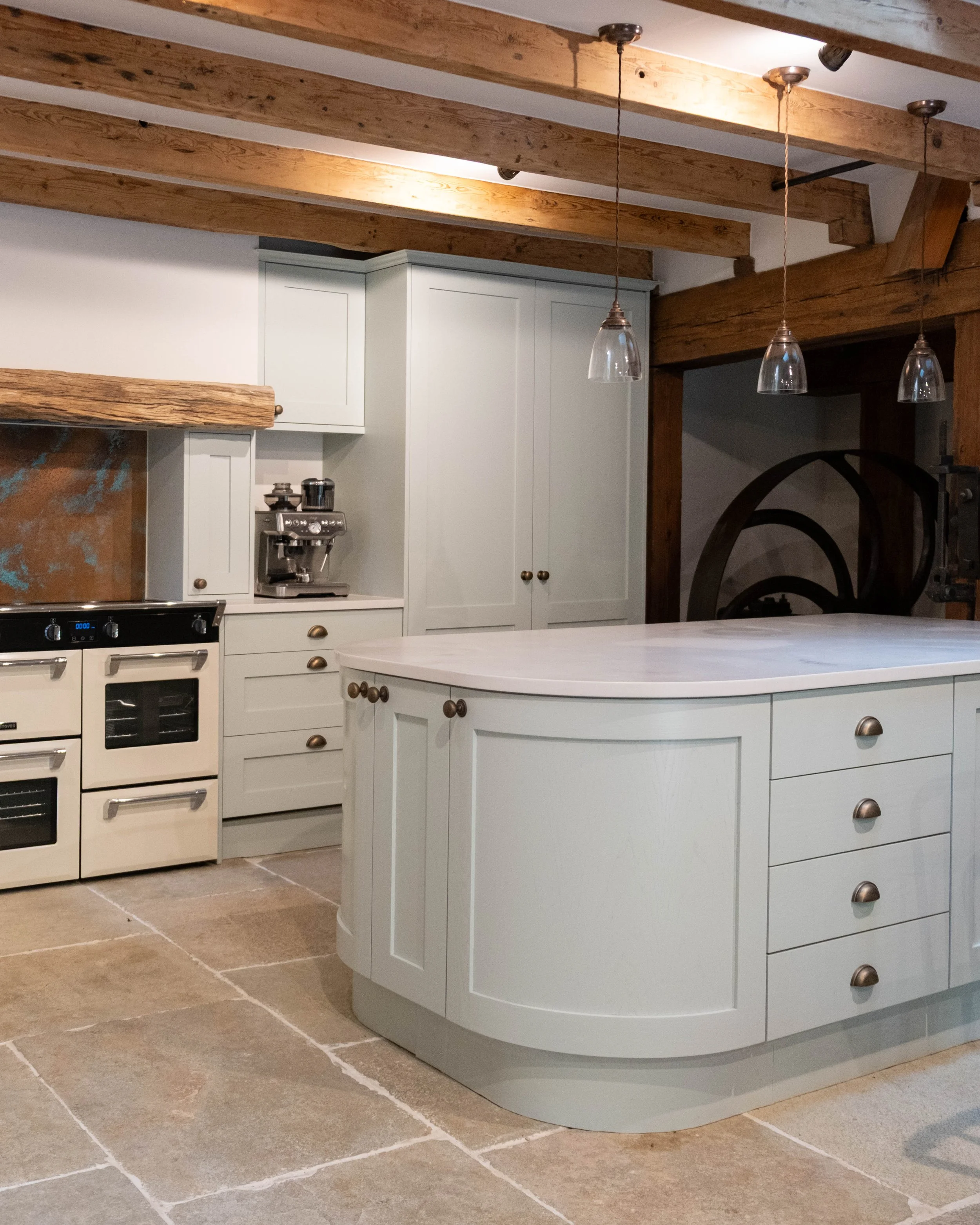 A kitchen with white cabinets, a vintage stove, exposed wooden beams on the ceiling, pendant lights, and a beige tiled floor.