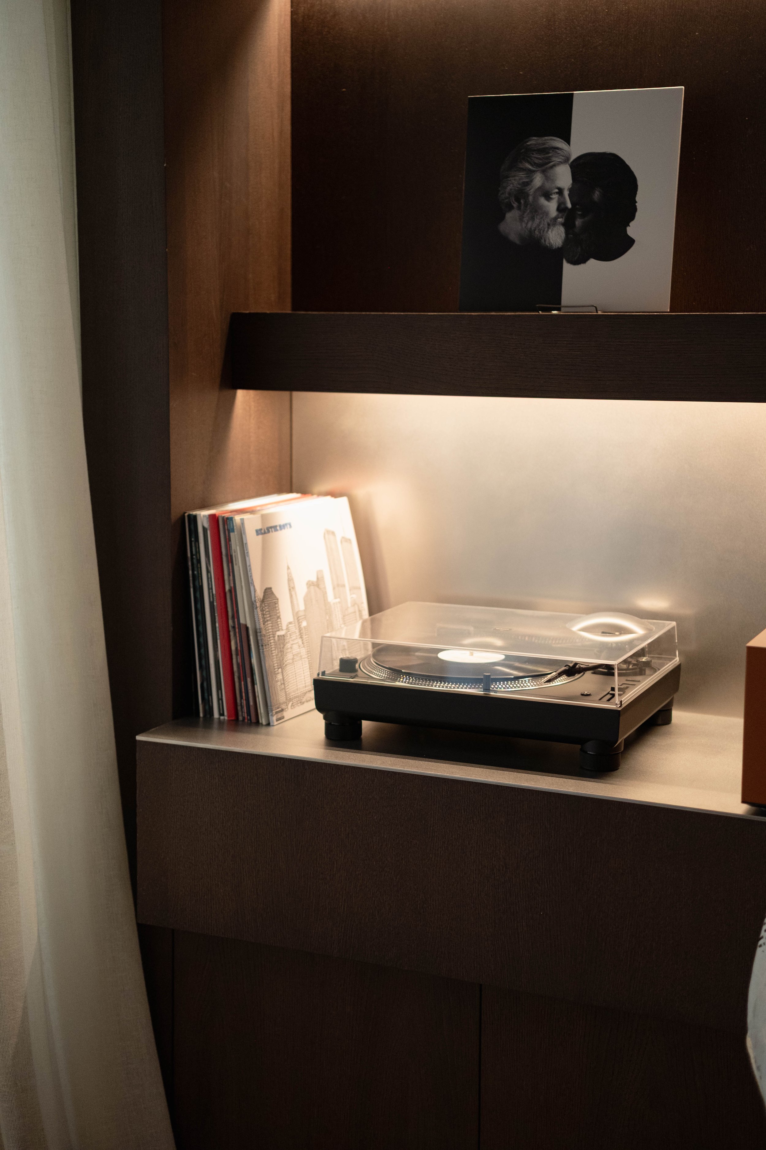 A turntable on a shelf with a stack of books and a framed cityscape picture behind it.