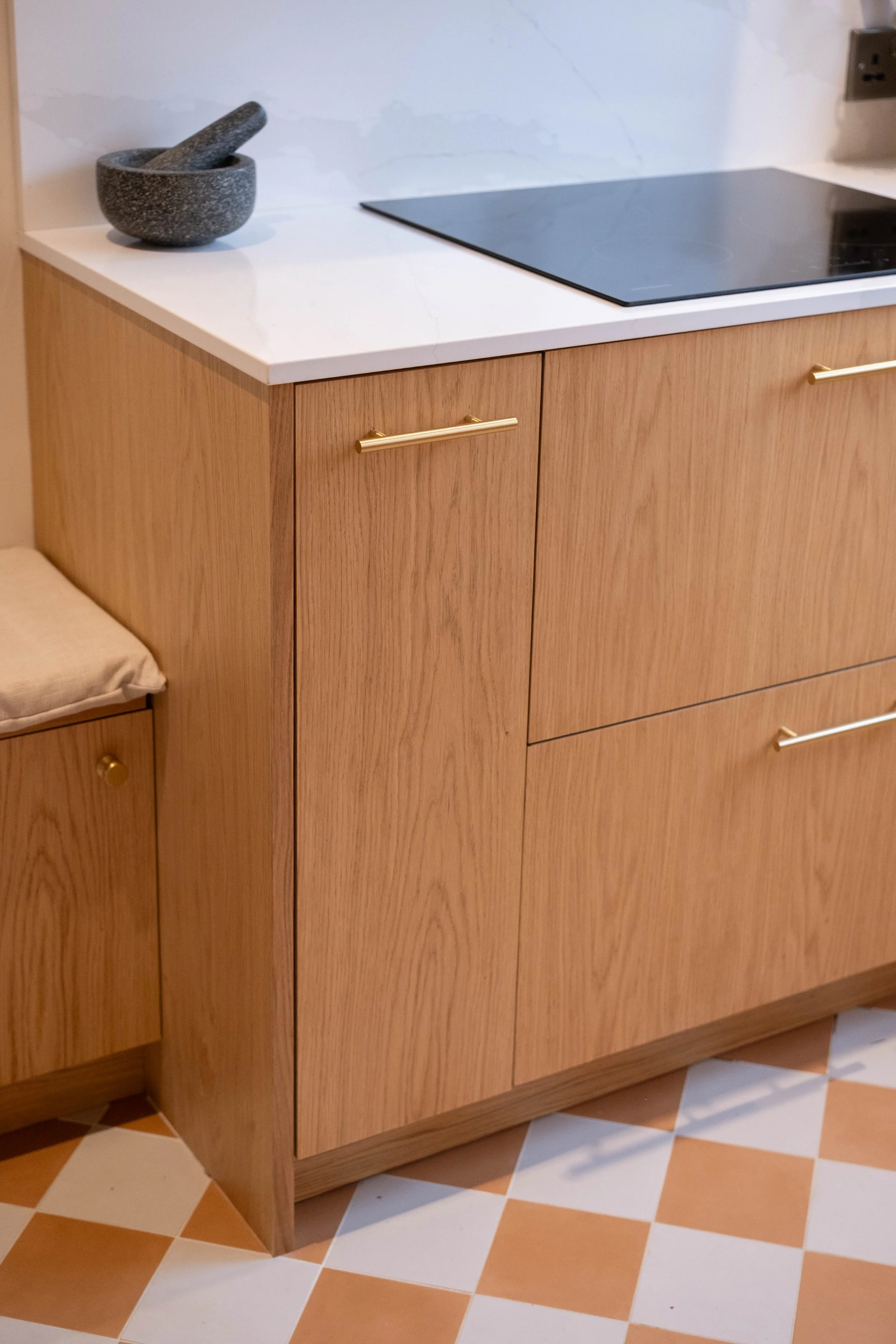 Wooden kitchen cabinet with brass handle beside a beige and white tiled floor, marble countertop, and a stone mortar and pestle on the countertop.