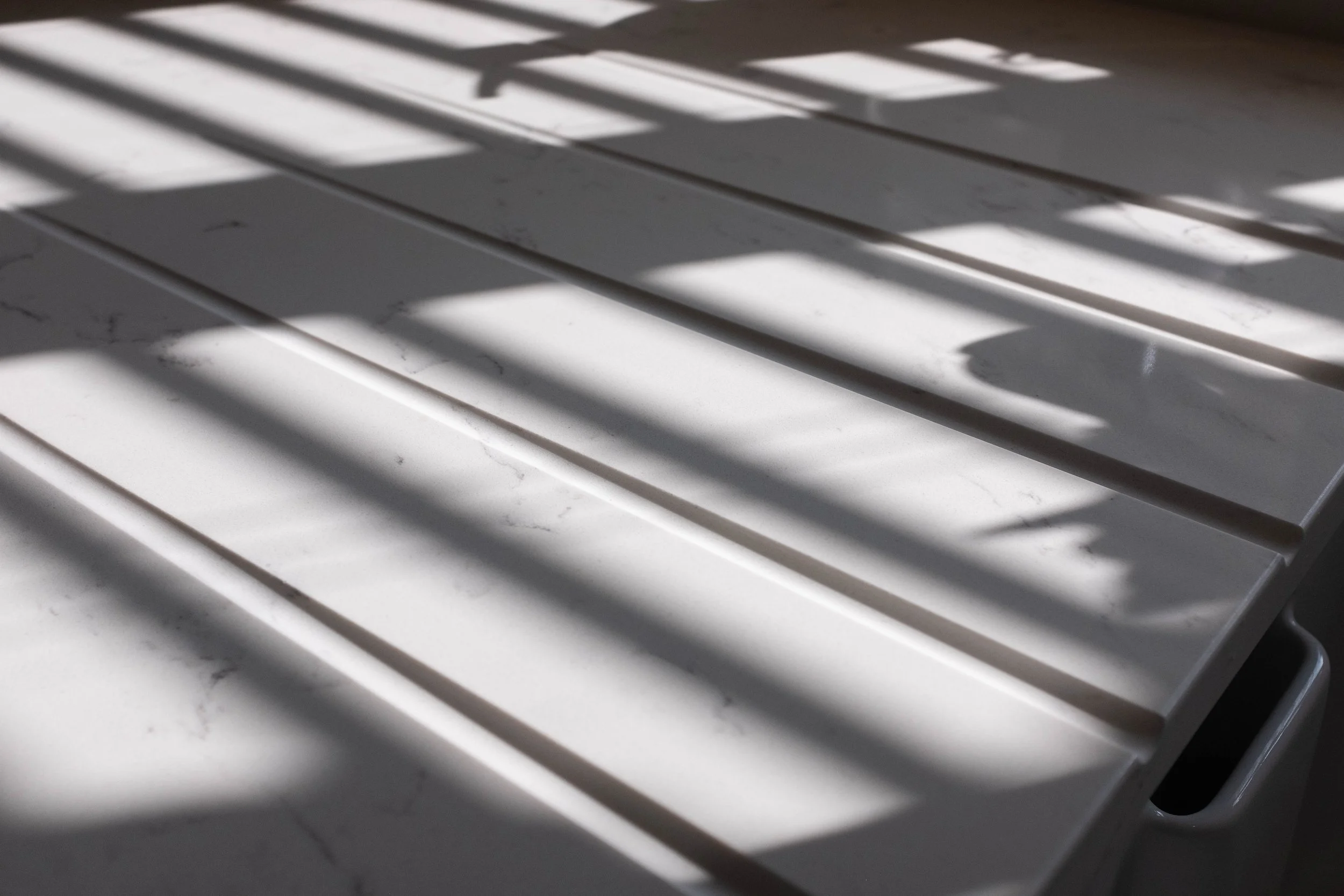 Shadows of window blinds cast on white slatted surface.