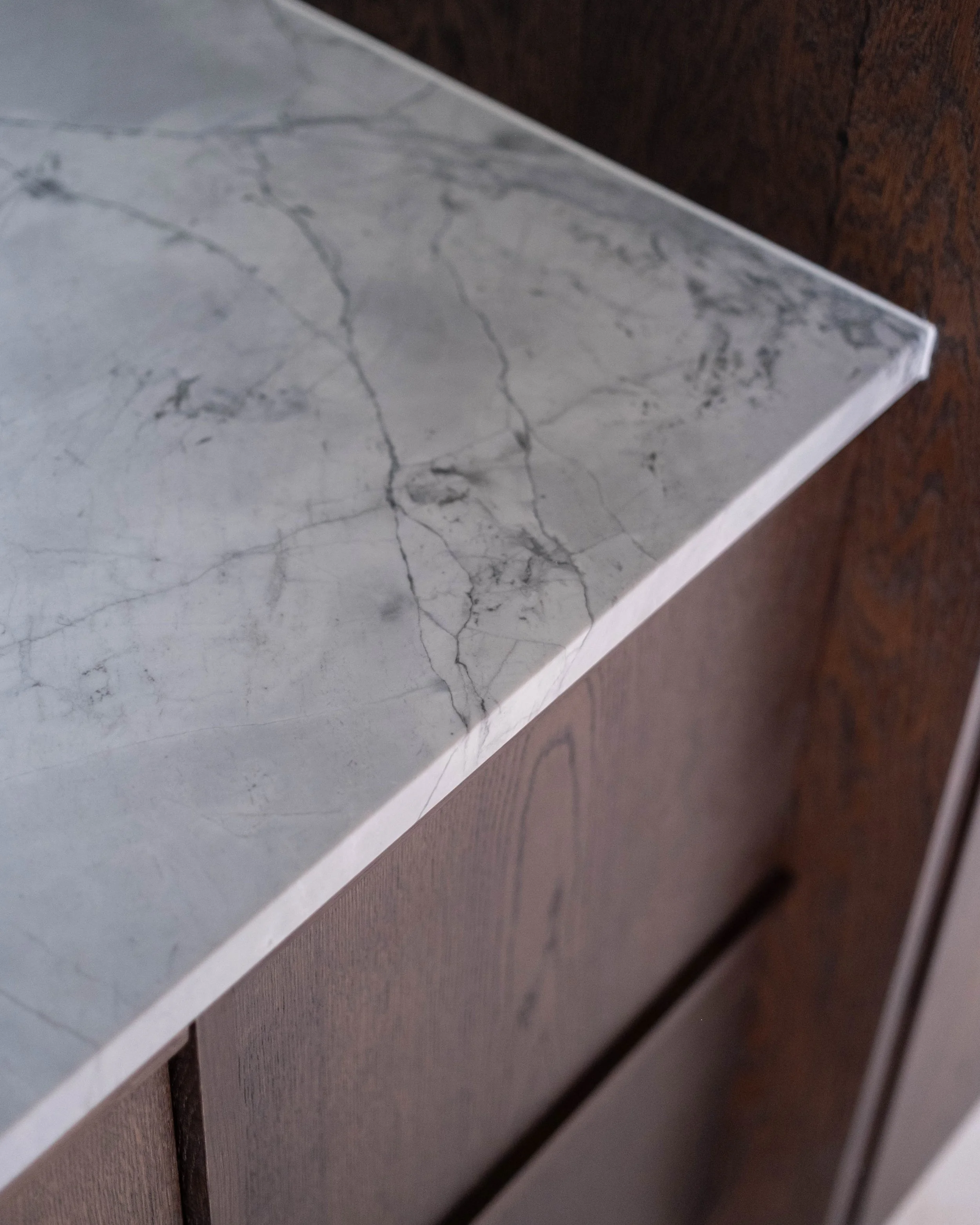 Close-up of a corner of a marble surface or countertop with gray veining, placed on a wooden surface.