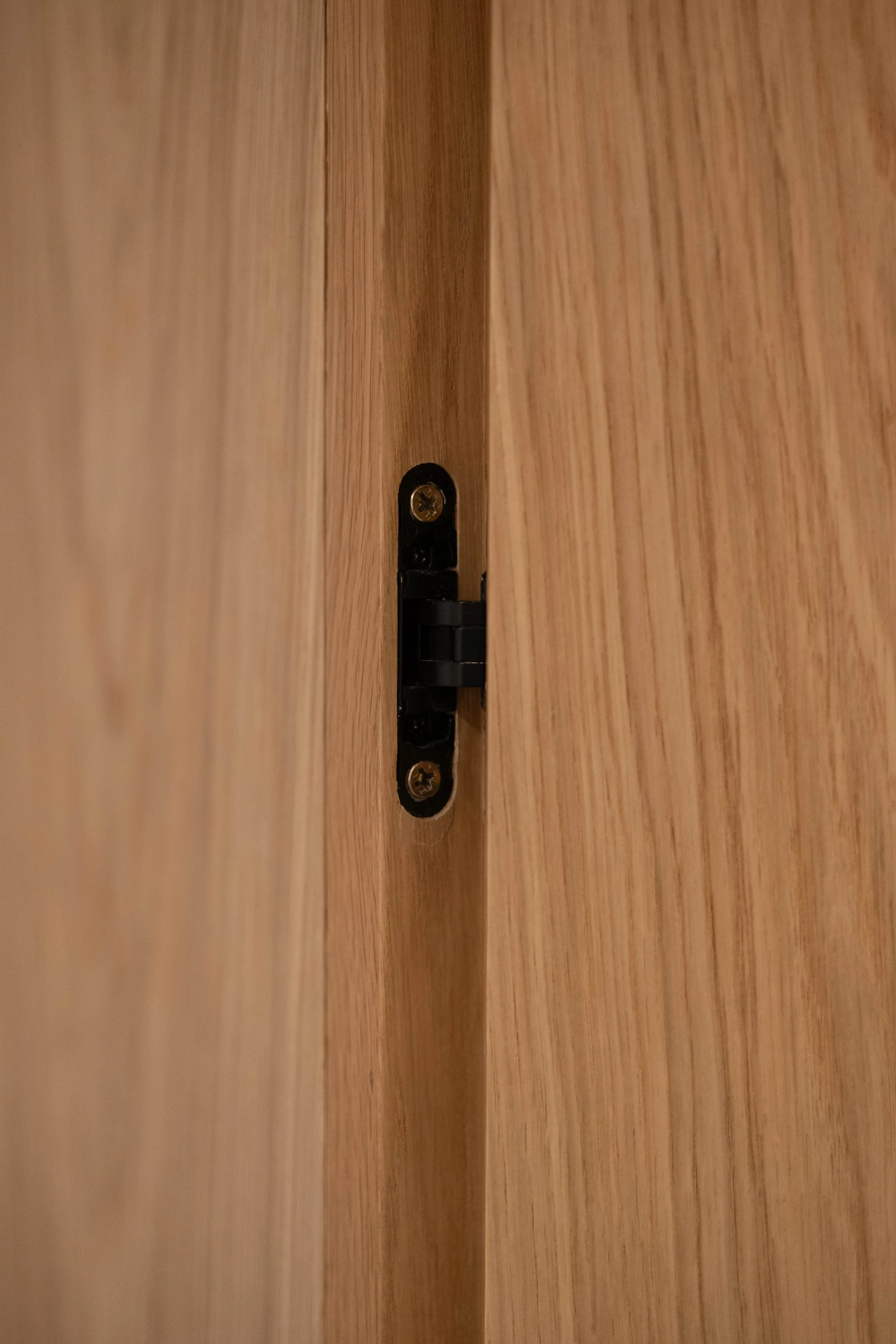 Close-up of a wooden door hinge with two screws, mounted on a wooden surface.