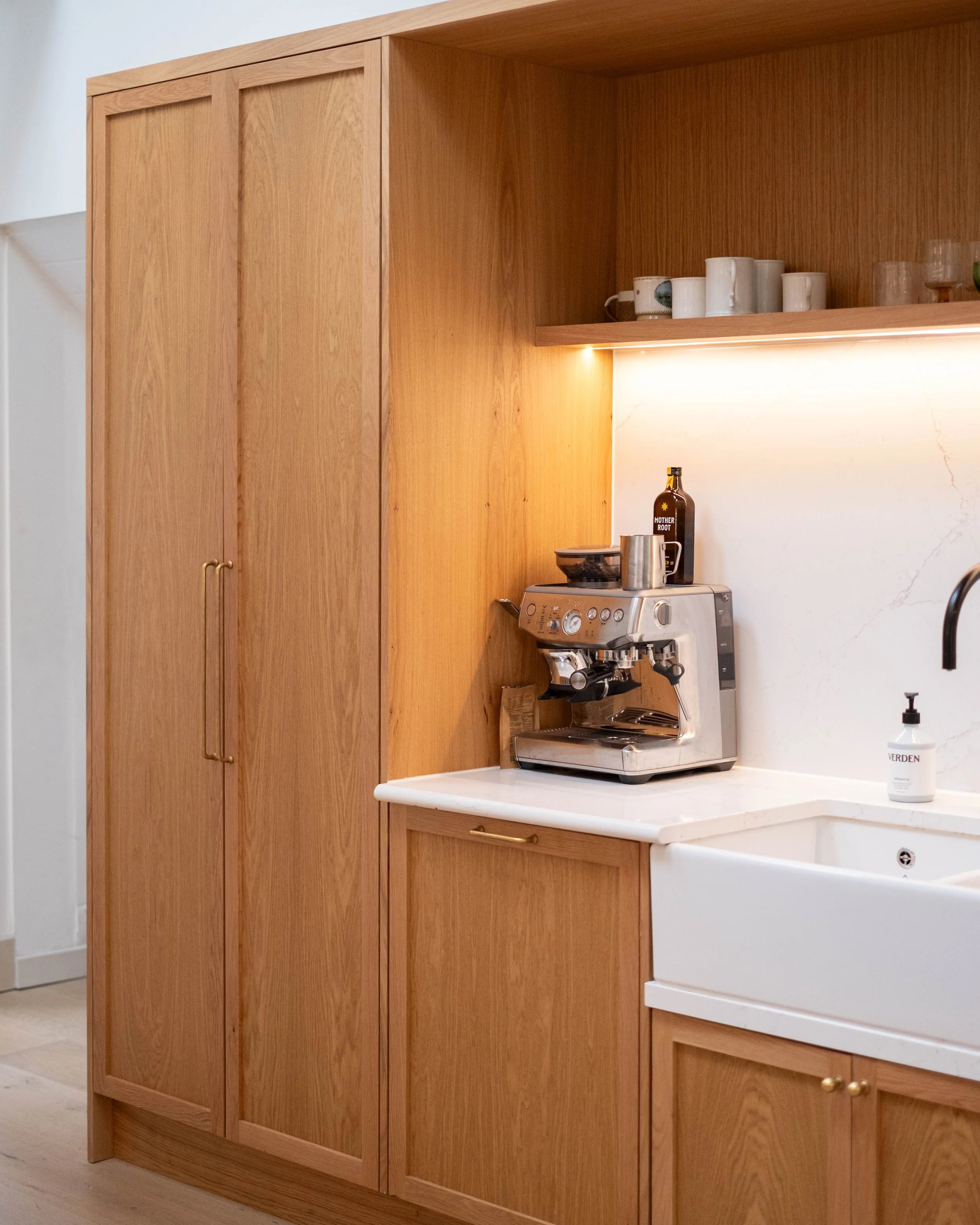 Kitchen with tall wooden cabinets, a white countertop, an espresso machine, a bottle labeled 'Mother Root,' and a soap dispenser.