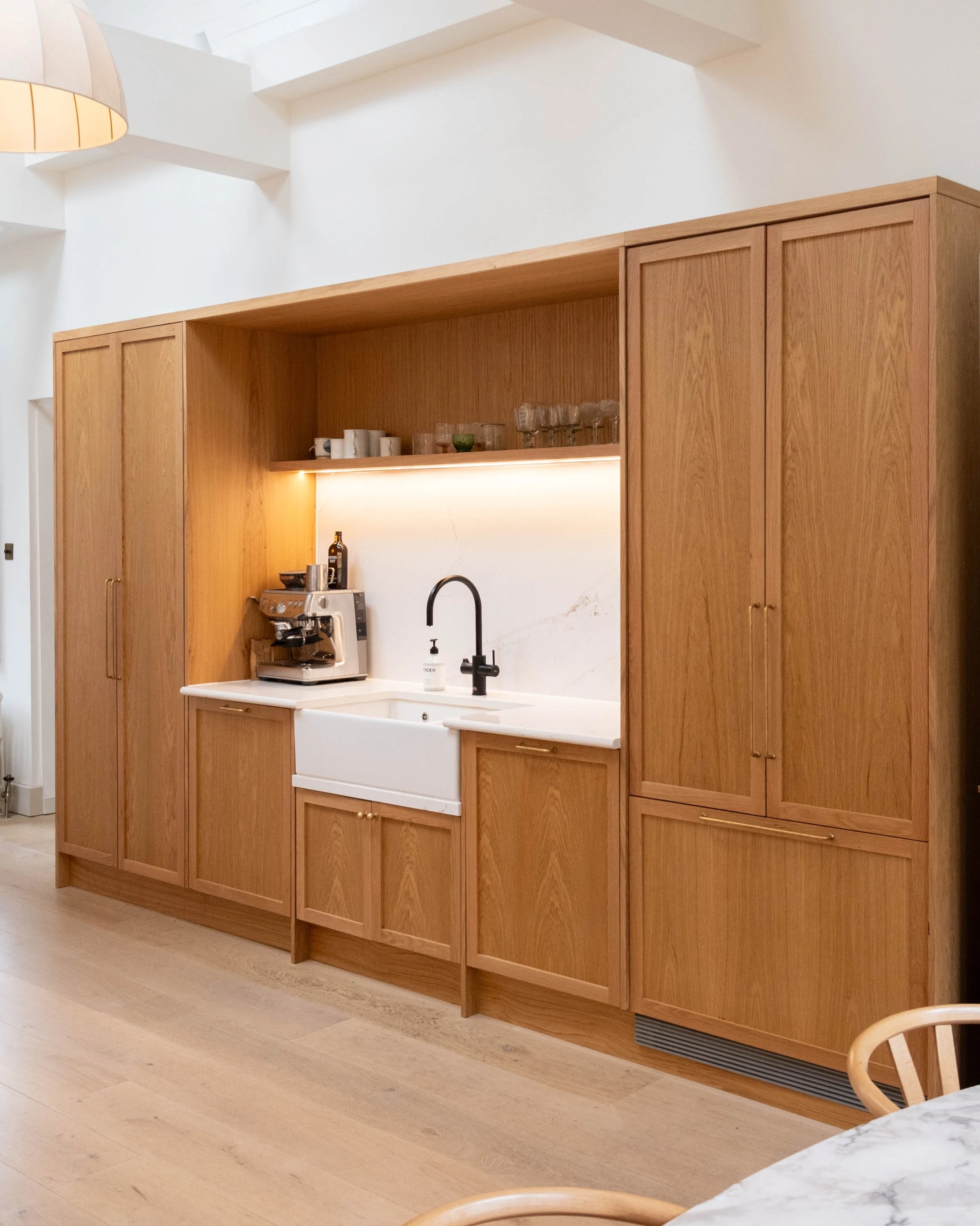 Modern kitchen with wooden cabinets, white marble countertop, black faucet, and coffee machine, illuminated with natural light from above.