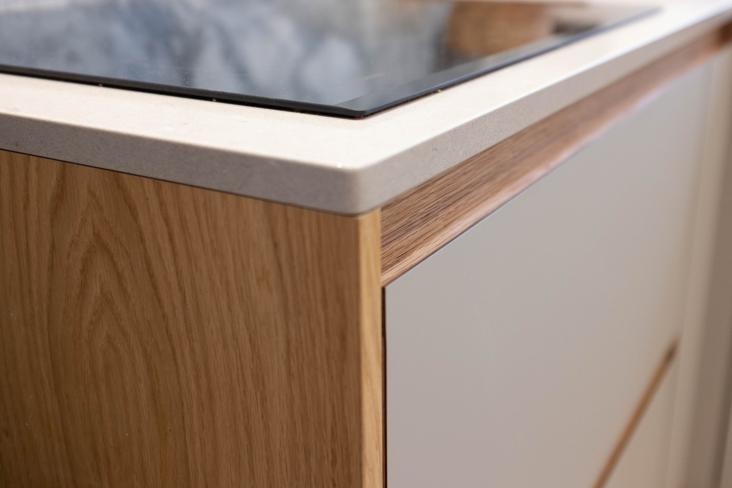 Close-up of a kitchen countertop with a stovetop, showing a section of the beige countertop, wooden cabinets, and a part of a white appliance.