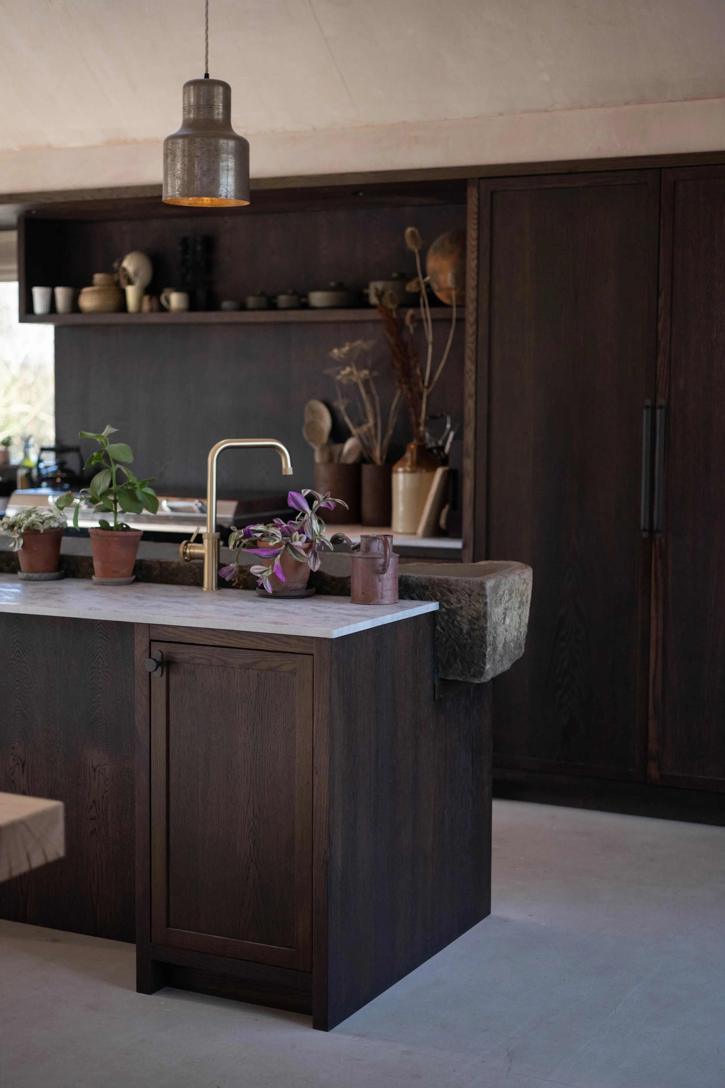 Kitchen with dark wood cabinets, a light marble island with potted plants, a gold faucet, and open shelves with dishes and decorations.