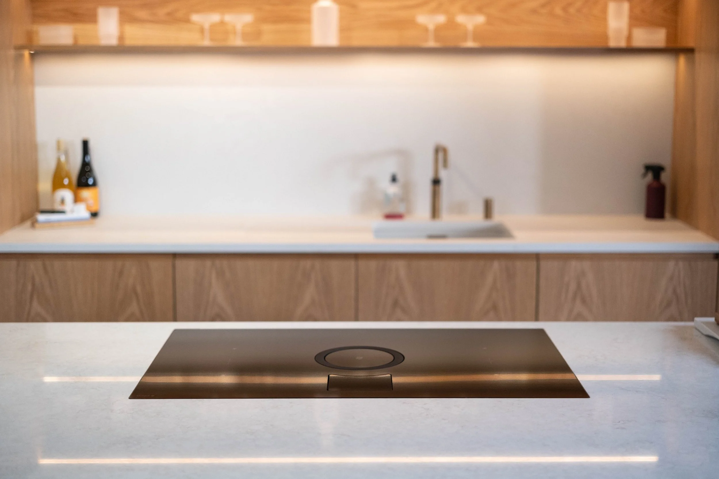 Modern kitchen with a built-in induction cooktop on a light-colored countertop, wood-paneled cabinets, and a white backsplash.