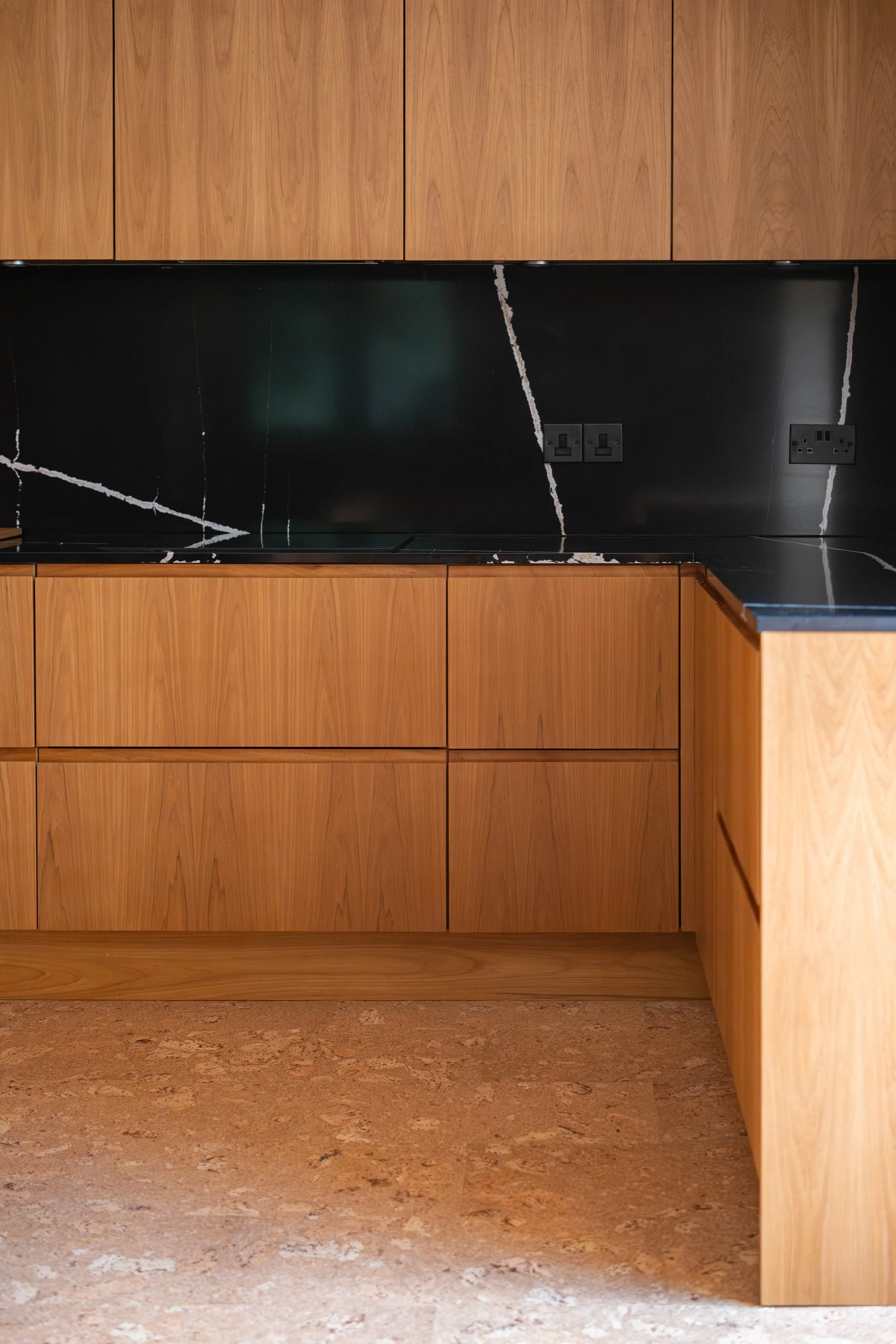 A kitchen with wooden cabinets, black marble backsplash with white veining, and visible electrical outlets.