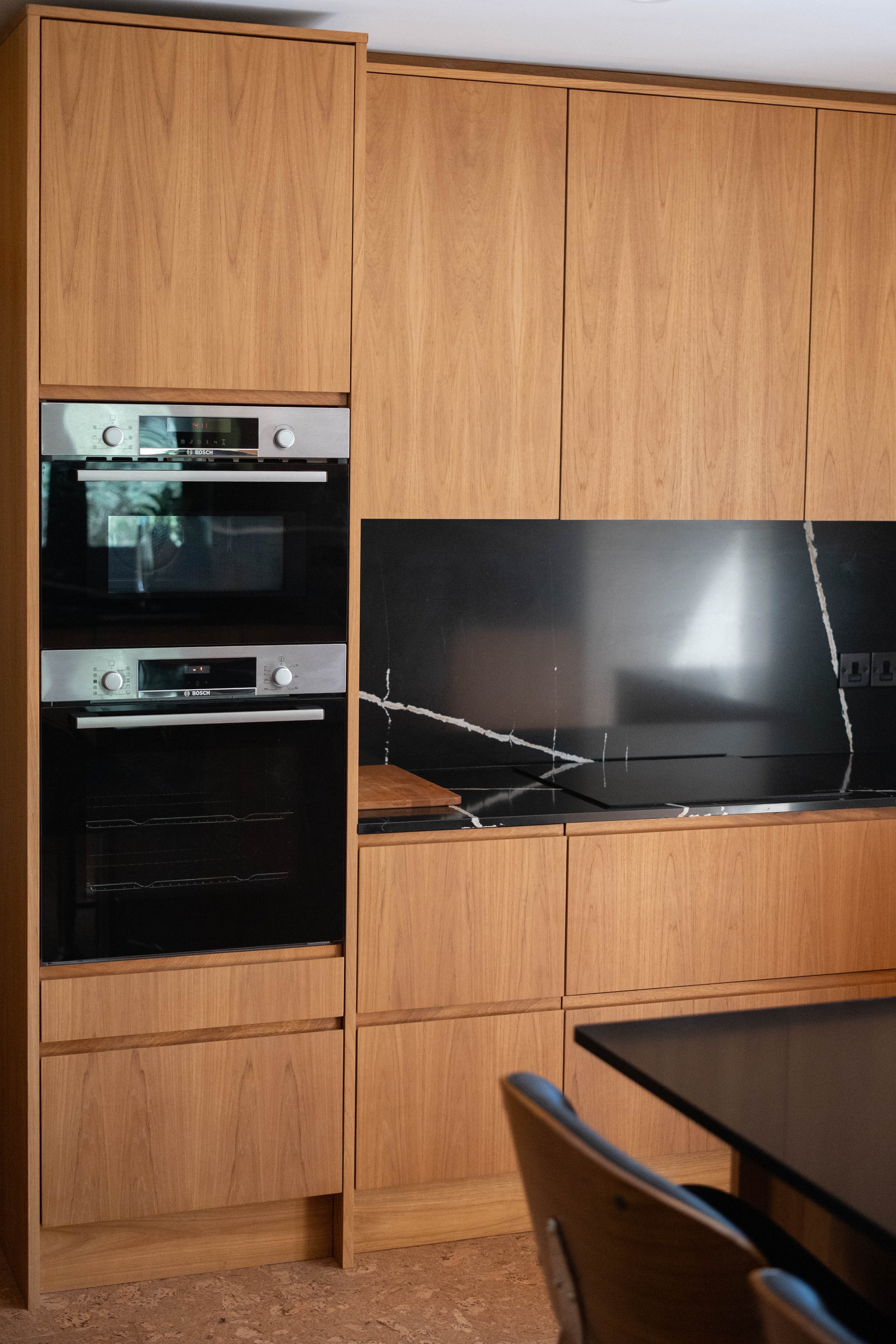 Kitchen with wooden cabinets, built-in Bosch oven, black marble backsplash, and black countertop.
