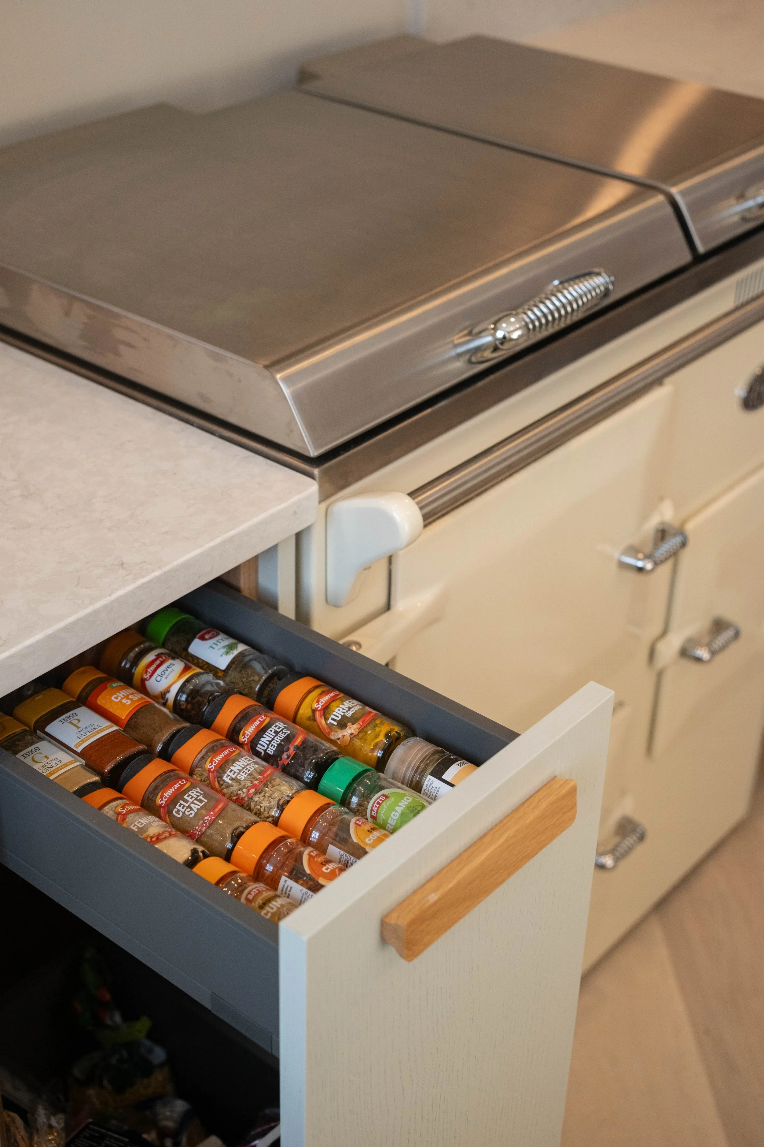 Open kitchen drawer filled with various spices in small glass bottles with orange lids, including sage, cinnamon, and turmeric.