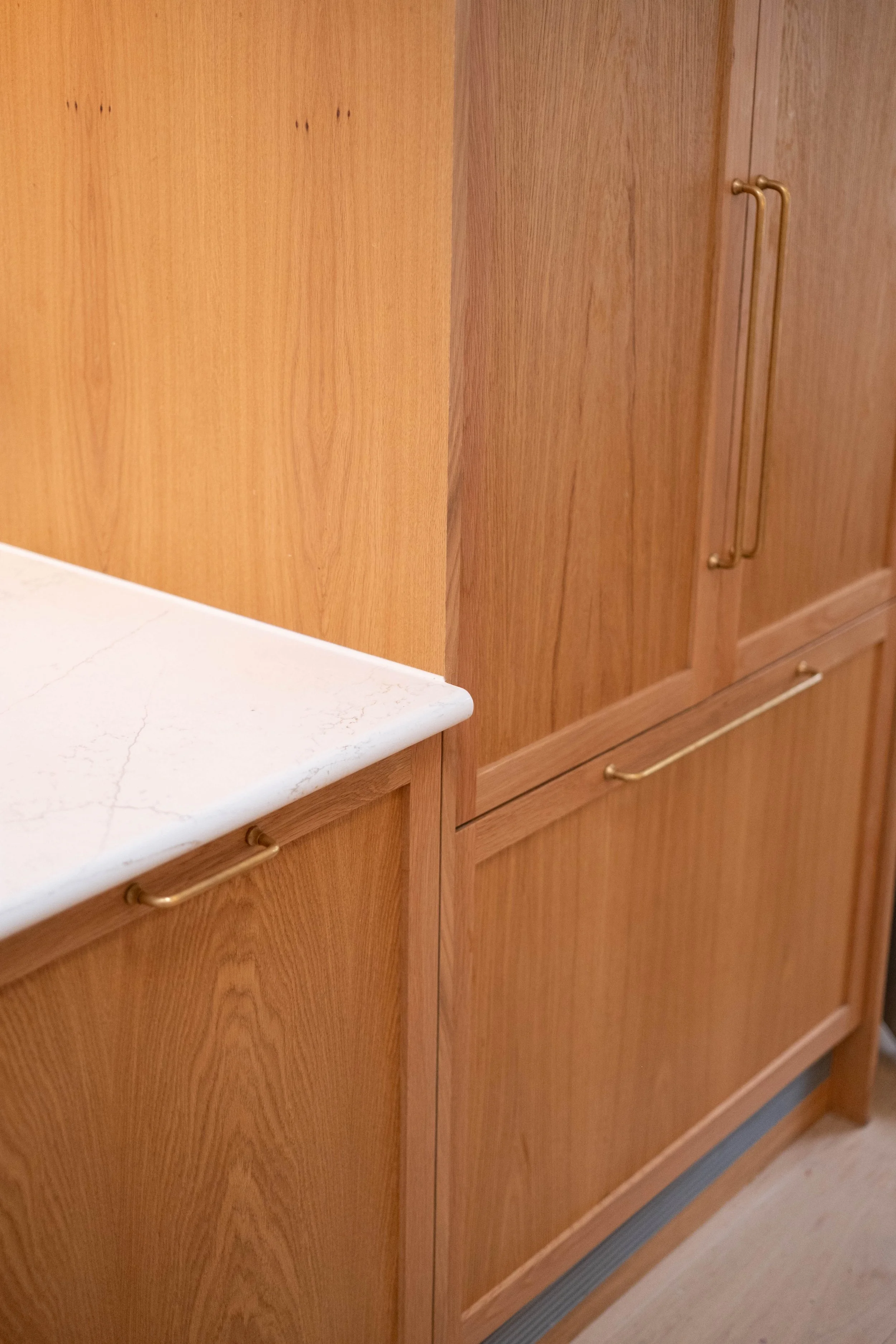 Wooden kitchen cabinets with gold handles and a white marble countertop.