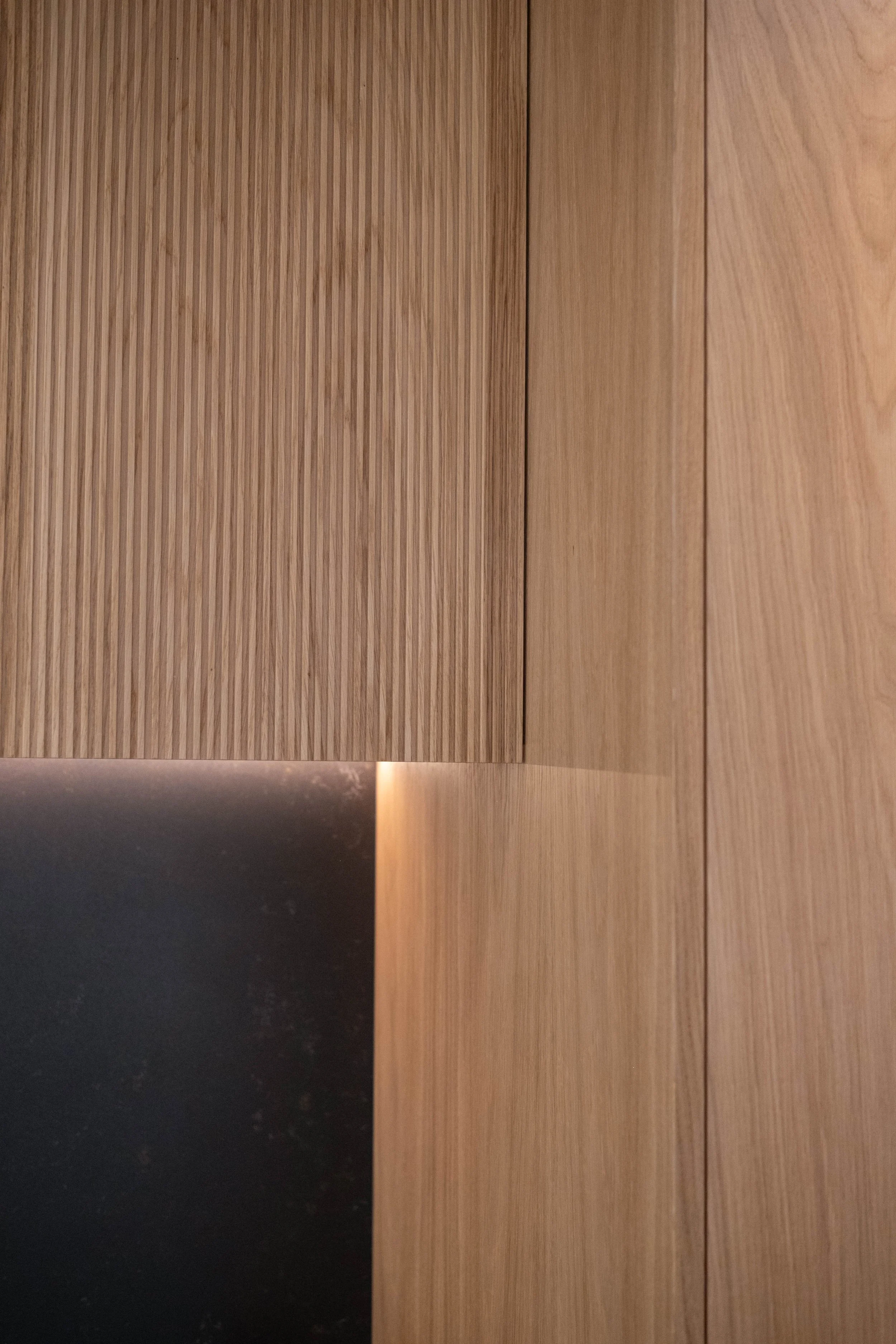 Close-up of wooden cabinet door with a corner meeting another door, showing wood grain patterns in light and dark tones.