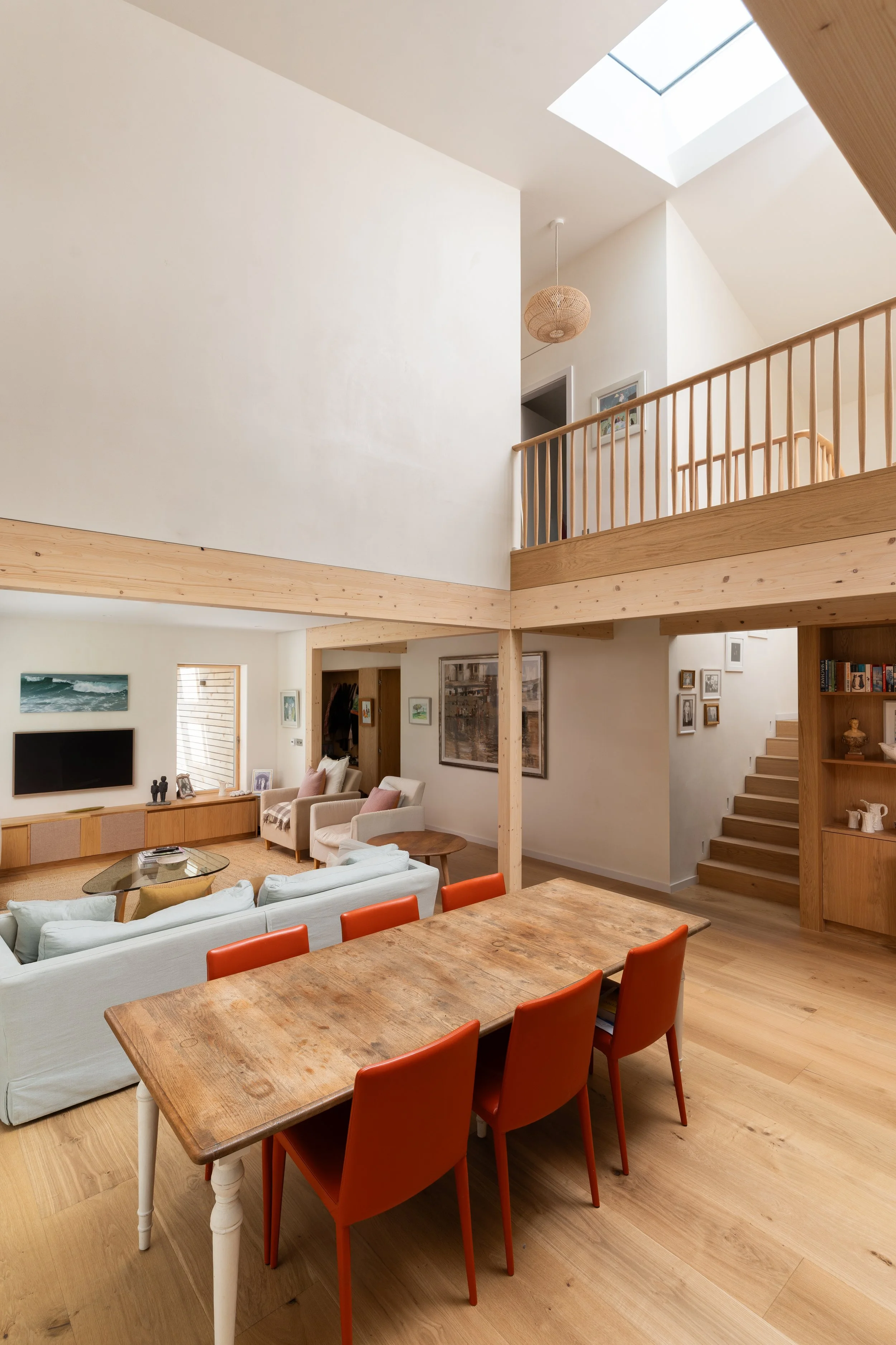 Open-concept living and dining area with wooden floors, a wooden staircase, and a ceiling with skylights, decorated with family photos, artwork, and a flat-screen TV.