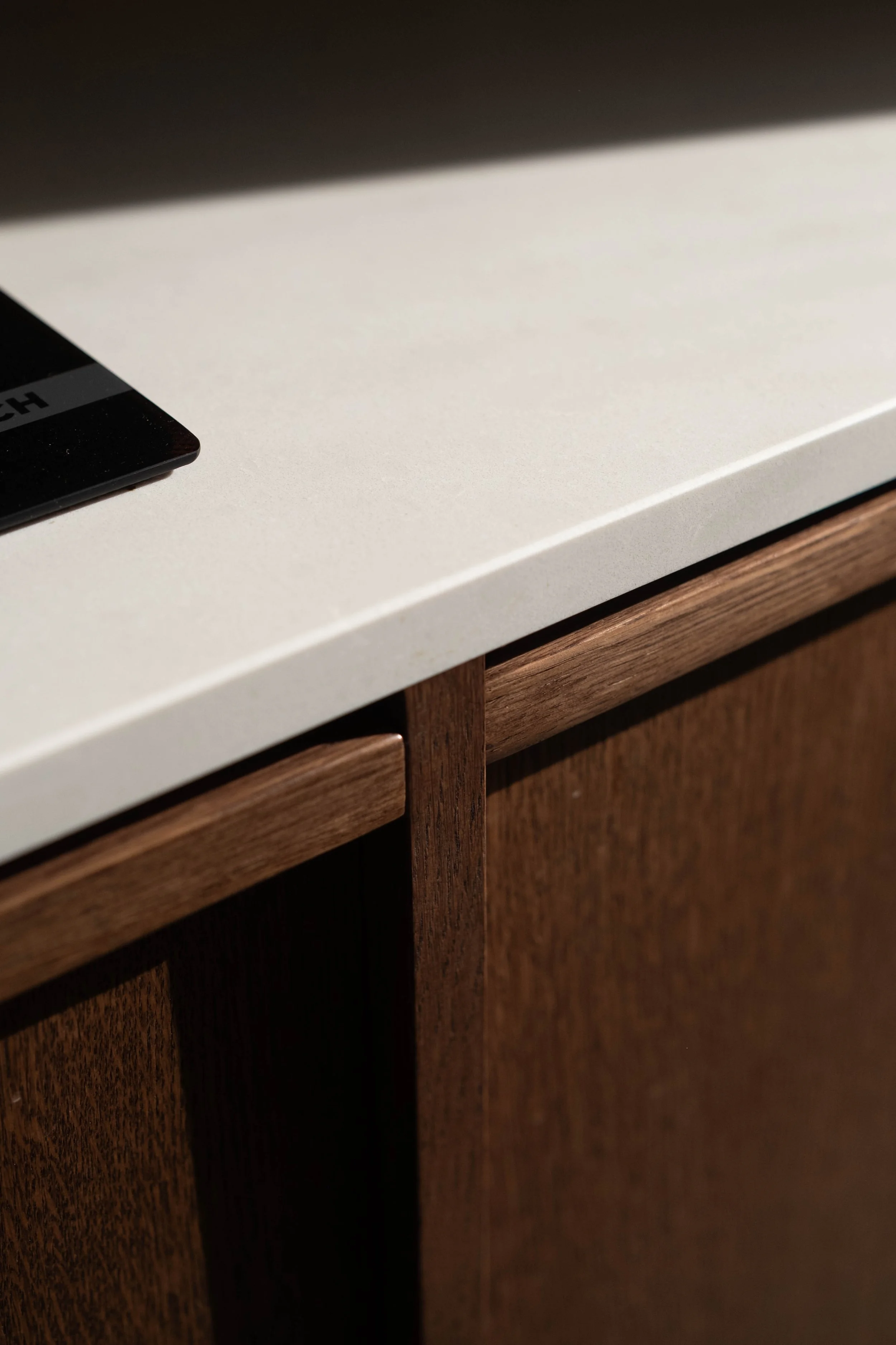 Close-up of a white countertop with a black electronic device partially visible in the corner and wooden cabinetry below.