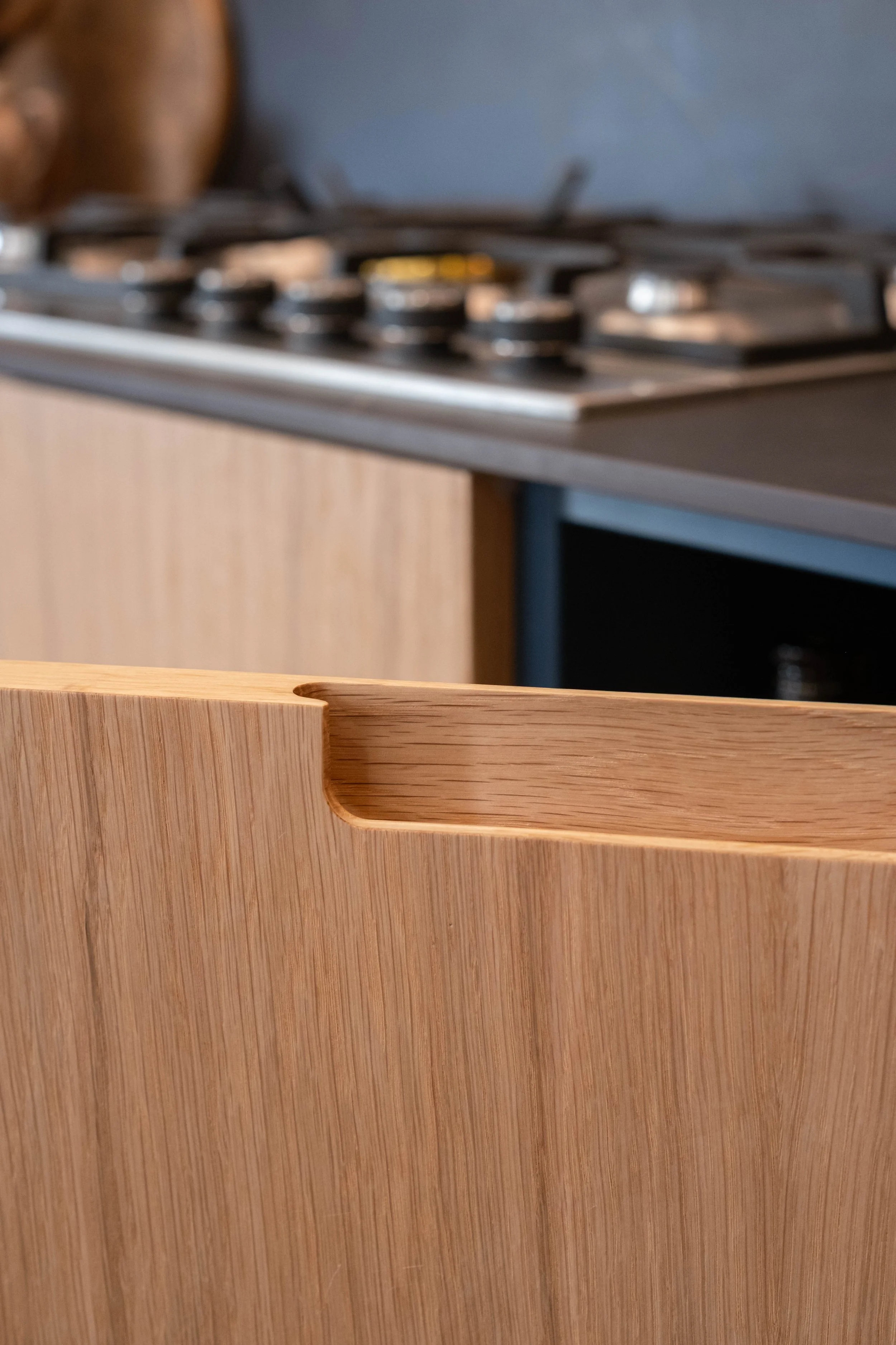 Close-up of a kitchen countertop with a wooden drawer in the foreground and a stovetop in the background.