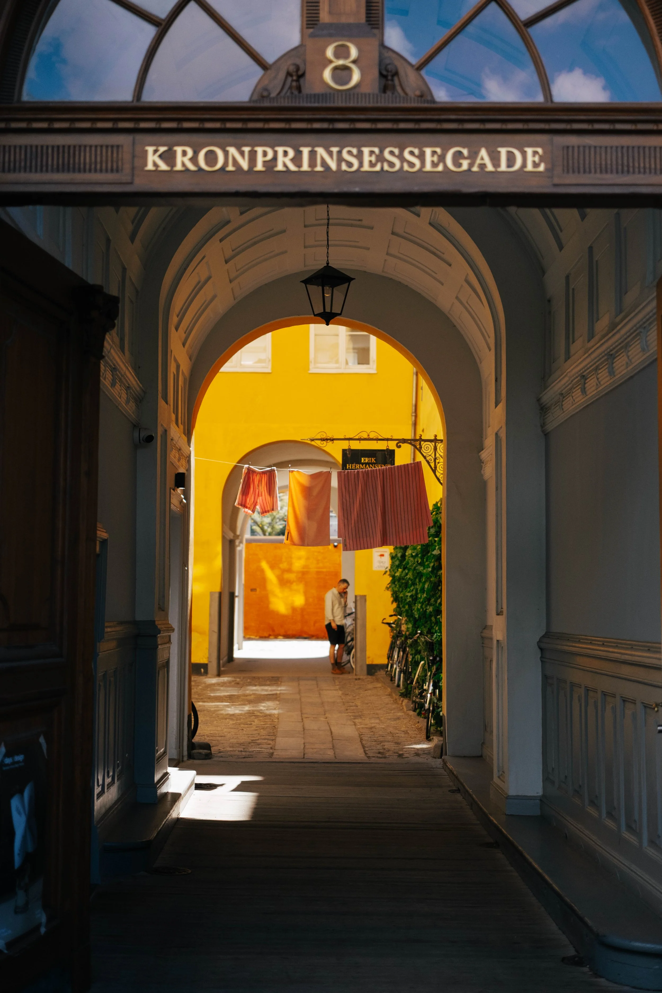 View through a decorative archway into a cobblestone street with colorful buildings, laundry hanging, and a man standing next to bicycles.