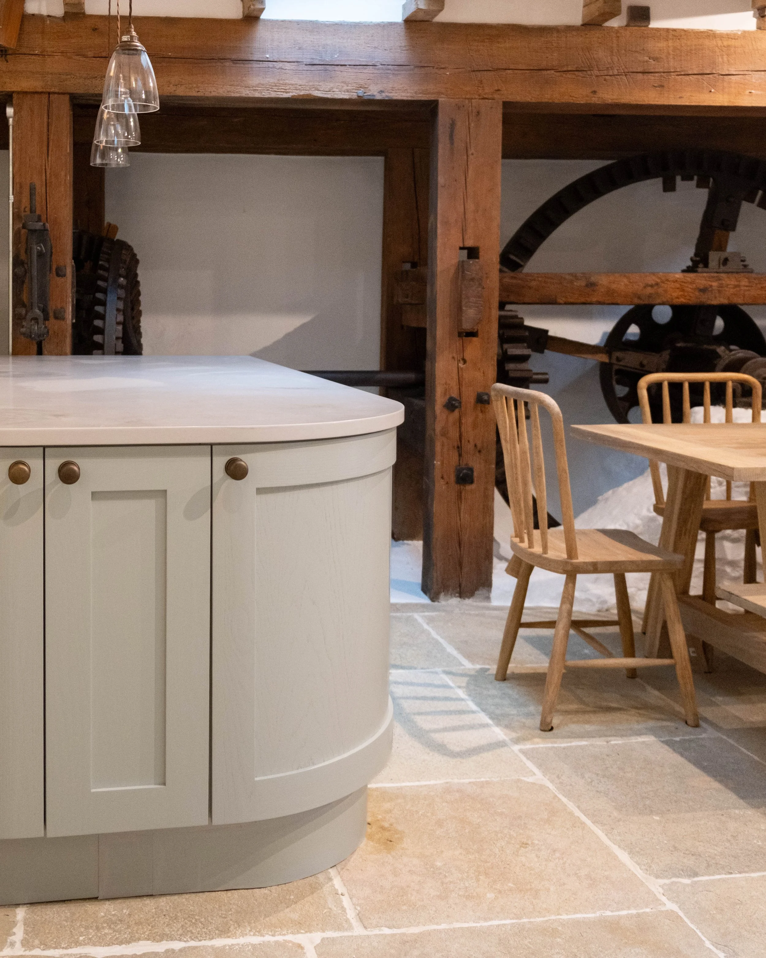 Close-up of a white kitchen island with wooden cabinets and pulls, with a wooden table and chairs in the background, and a large wooden beam supporting the ceiling.