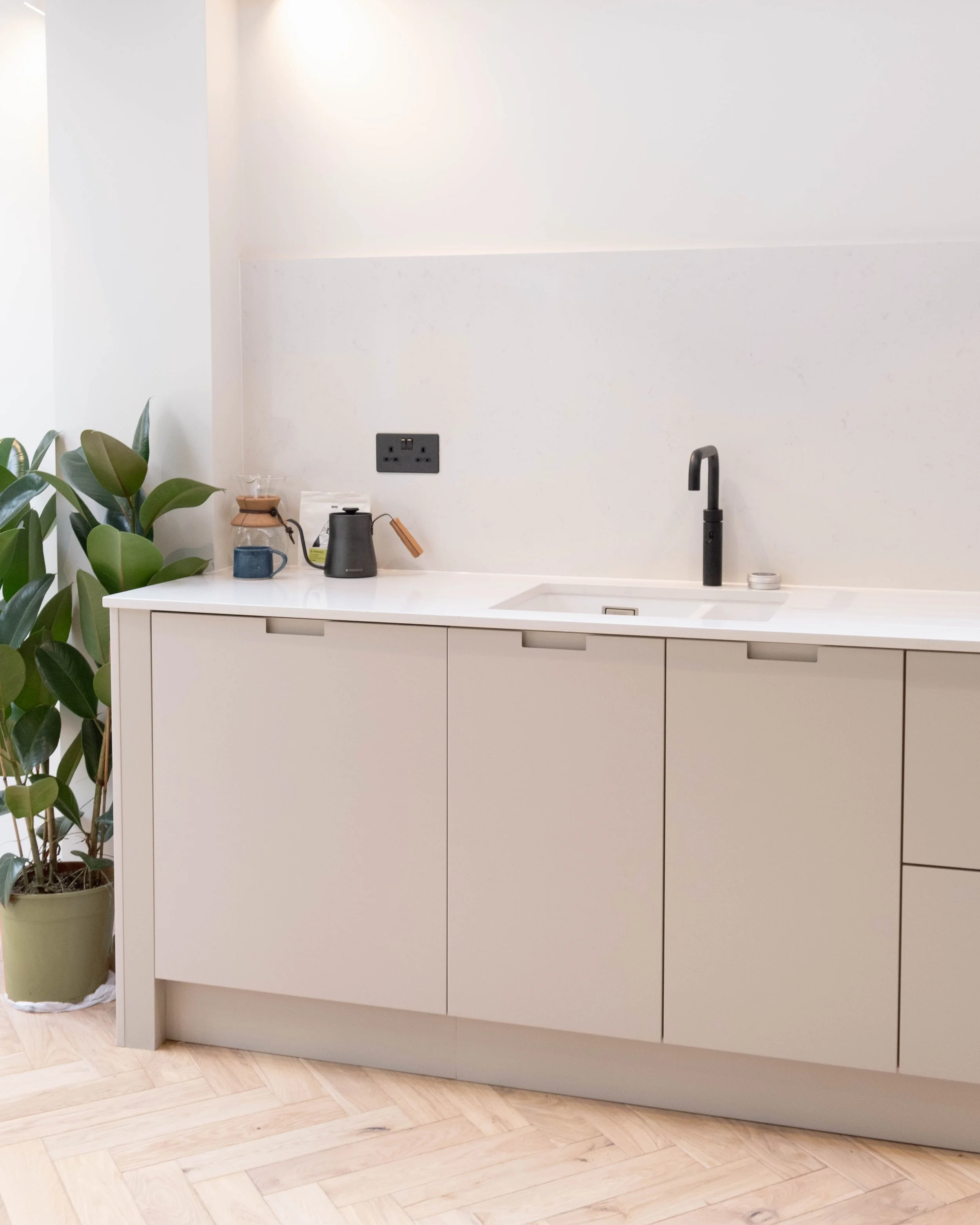 Modern kitchen with white cabinetry, black faucet, potted plant, and small kitchen appliances on the countertop.