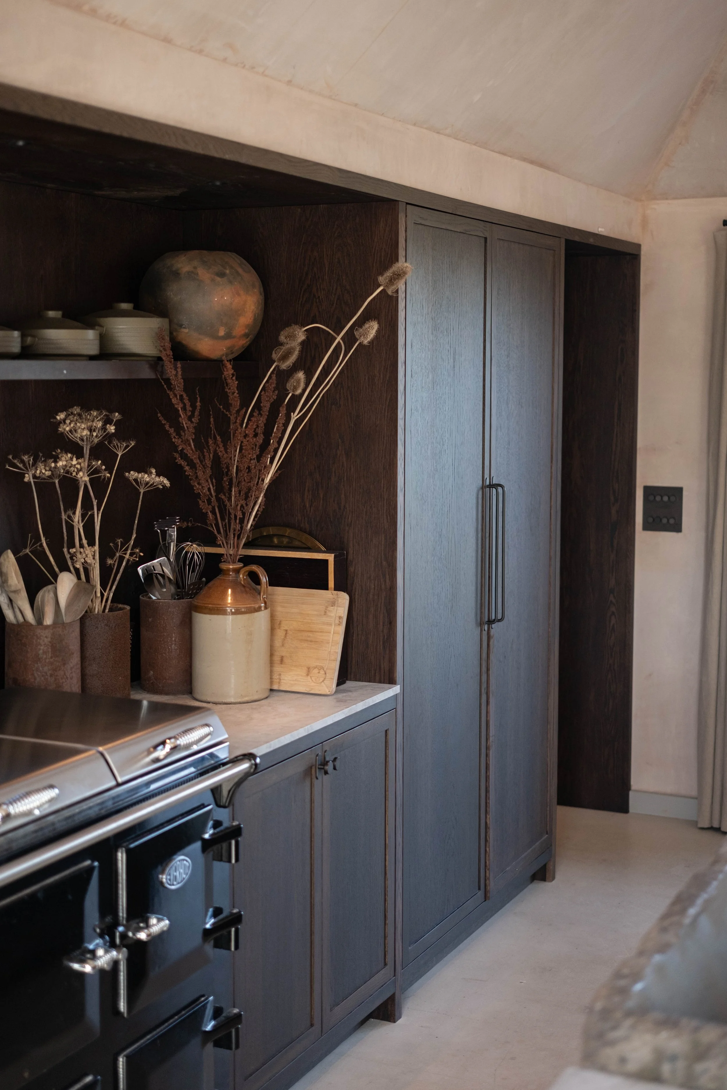 A kitchen with dark wood cabinets, a marble countertop, and decorative vases with dried flowers, next to a stove.
