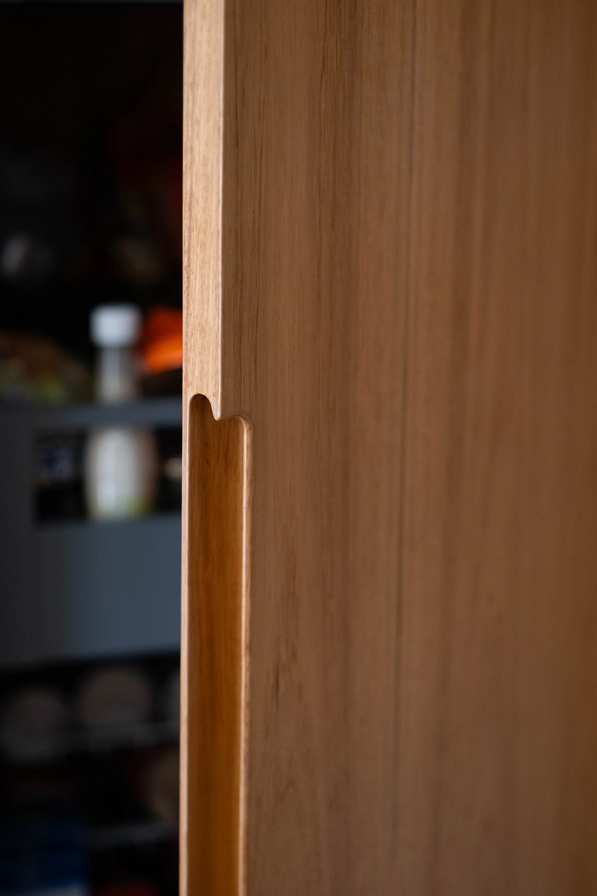 Close-up of a wooden furniture edge with a small notch cut in it, blurred background with bottles.