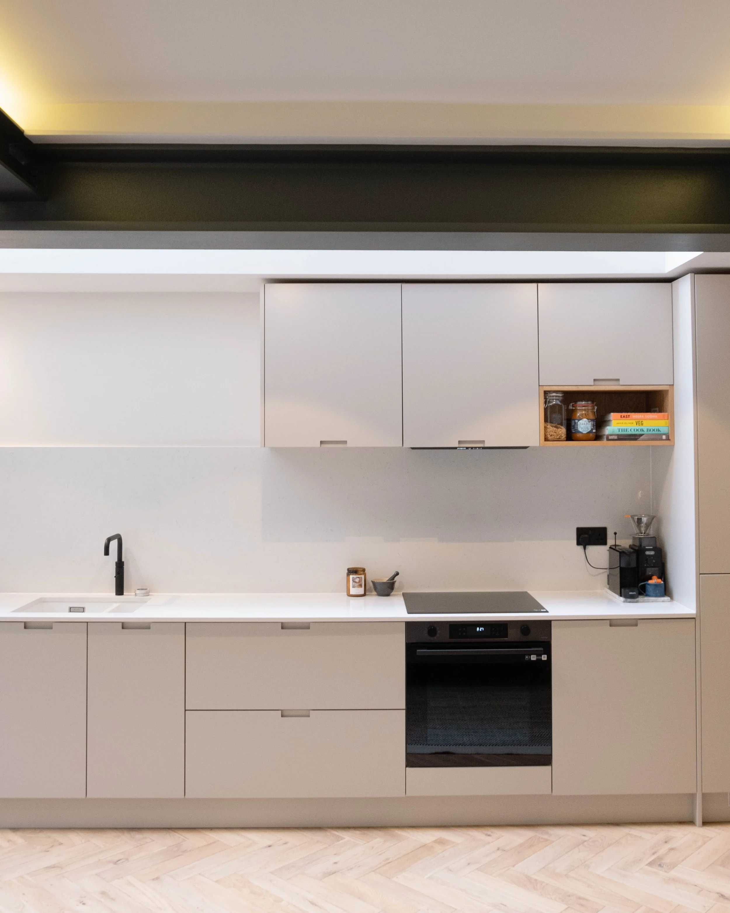 Modern kitchen with white cabinets, a built-in oven, black range hood, white countertop, black faucet, and light wood flooring.