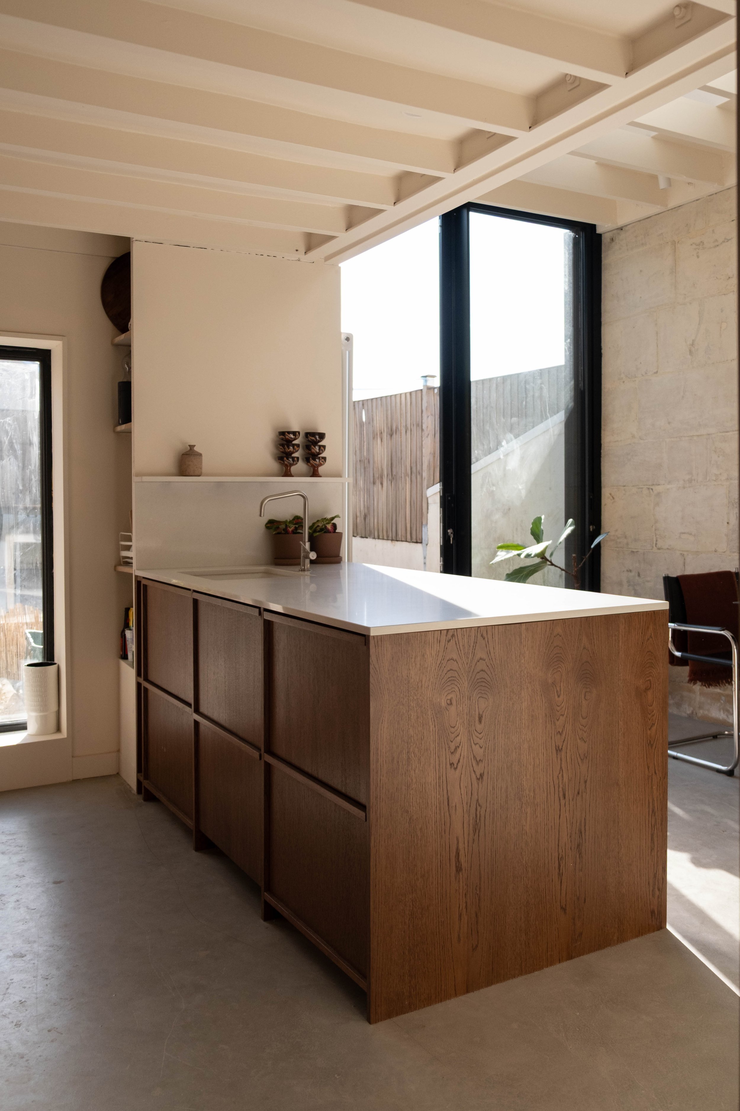 A kitchen island with wooden drawers and a white countertop, situated in a modern kitchen with large window and natural light.