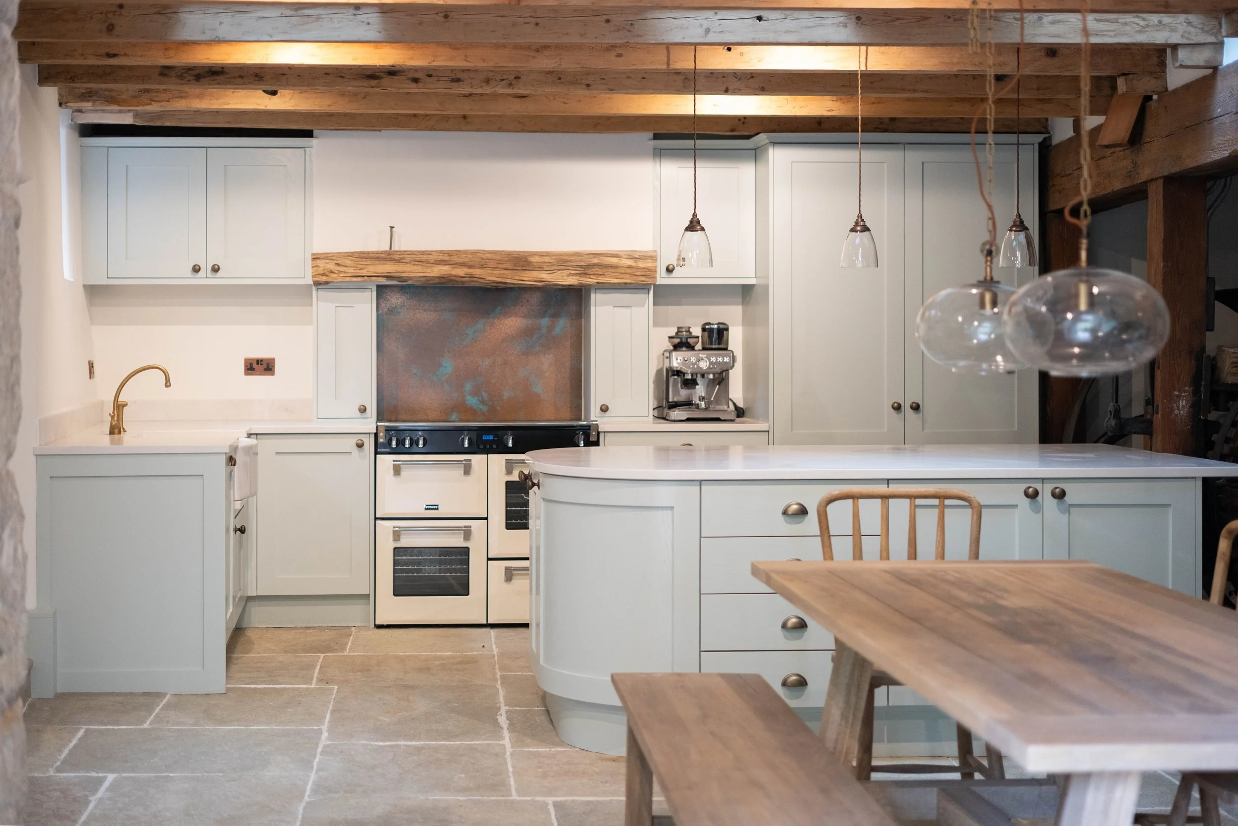 A modern kitchen with white cabinets, stainless steel appliances, wooden ceiling beams, and a wooden dining table with chairs.