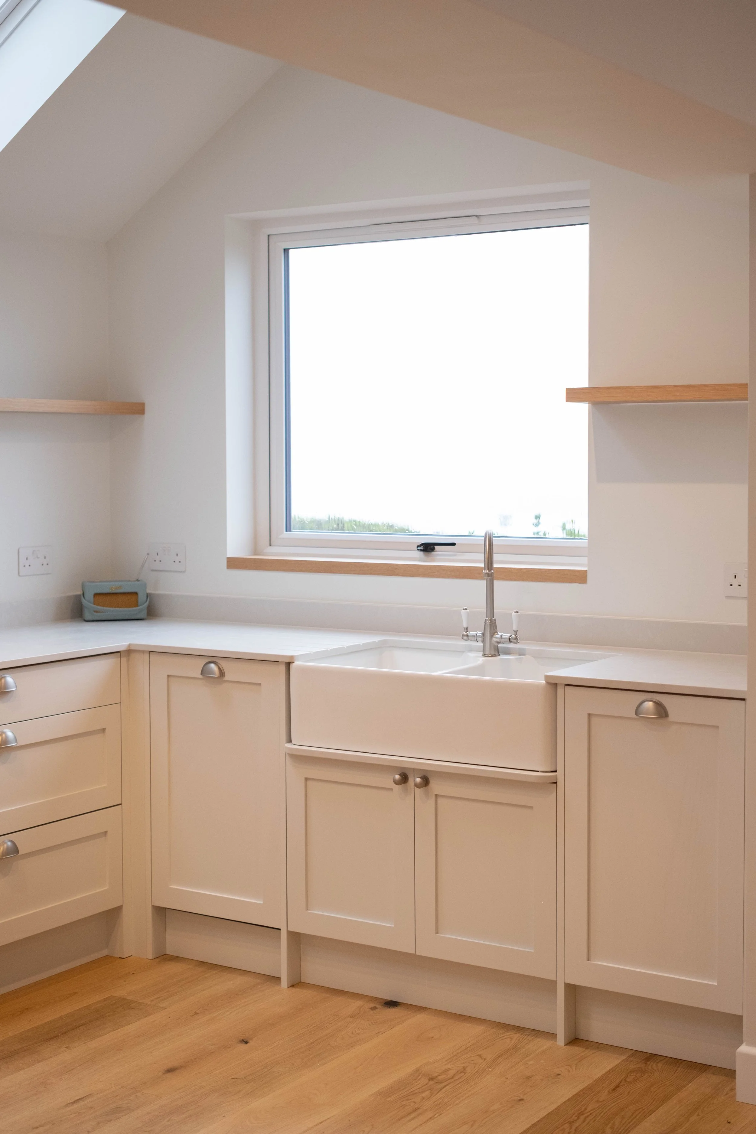 A kitchen with white cabinets, a farmhouse sink, a window above the sink, and wooden flooring.