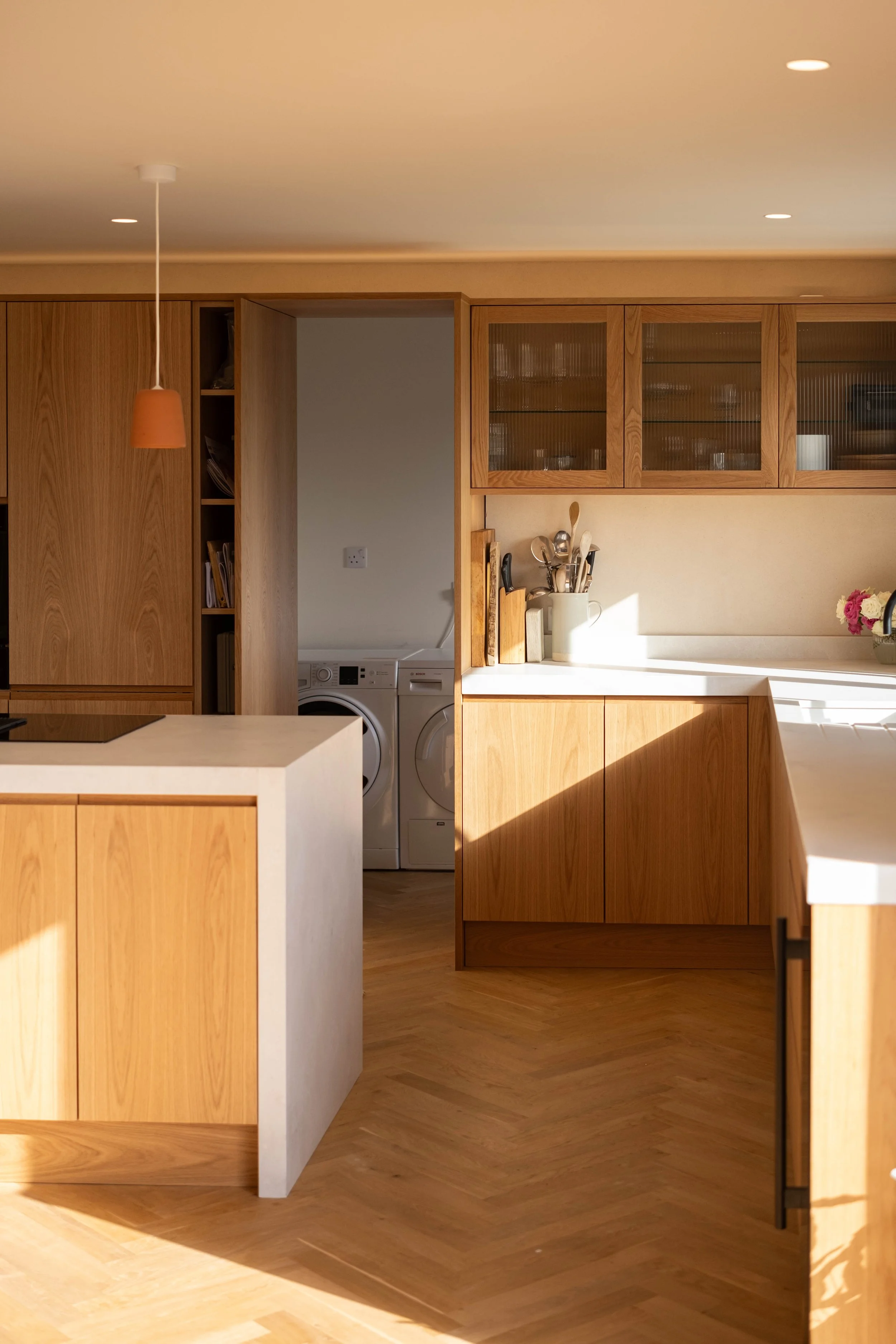 A modern kitchen with wooden cabinets, a white countertop, and a laundry area with washing machine and dryer visible through an open doorway.