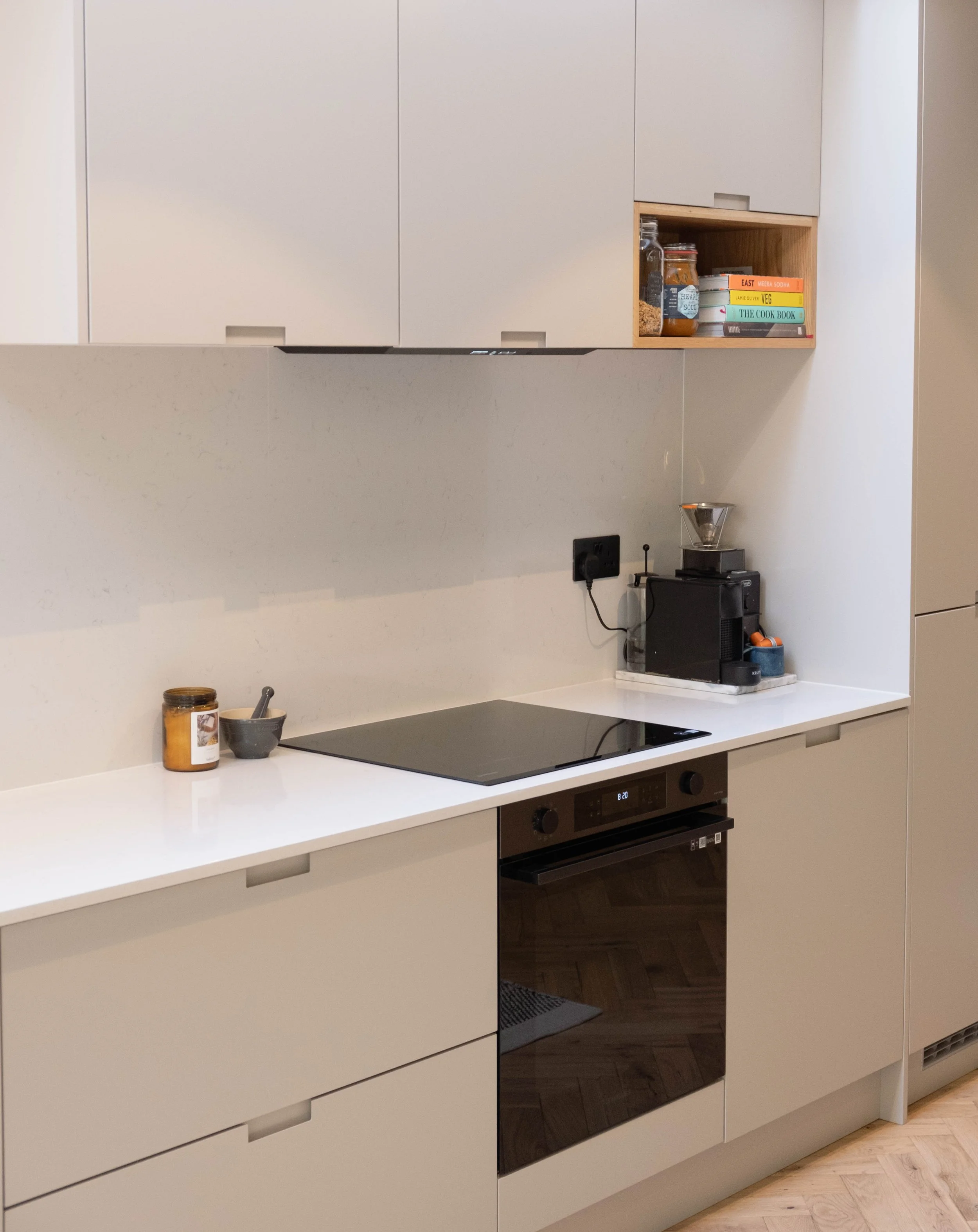 Modern kitchen with white cabinets, black stovetop, built-in oven, and a small countertop with jars and bowls.