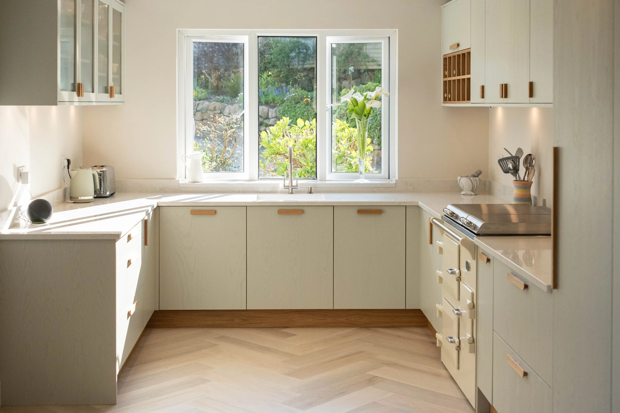 Bright kitchen with white cabinets, a window looking out to a garden, and various kitchen appliances.