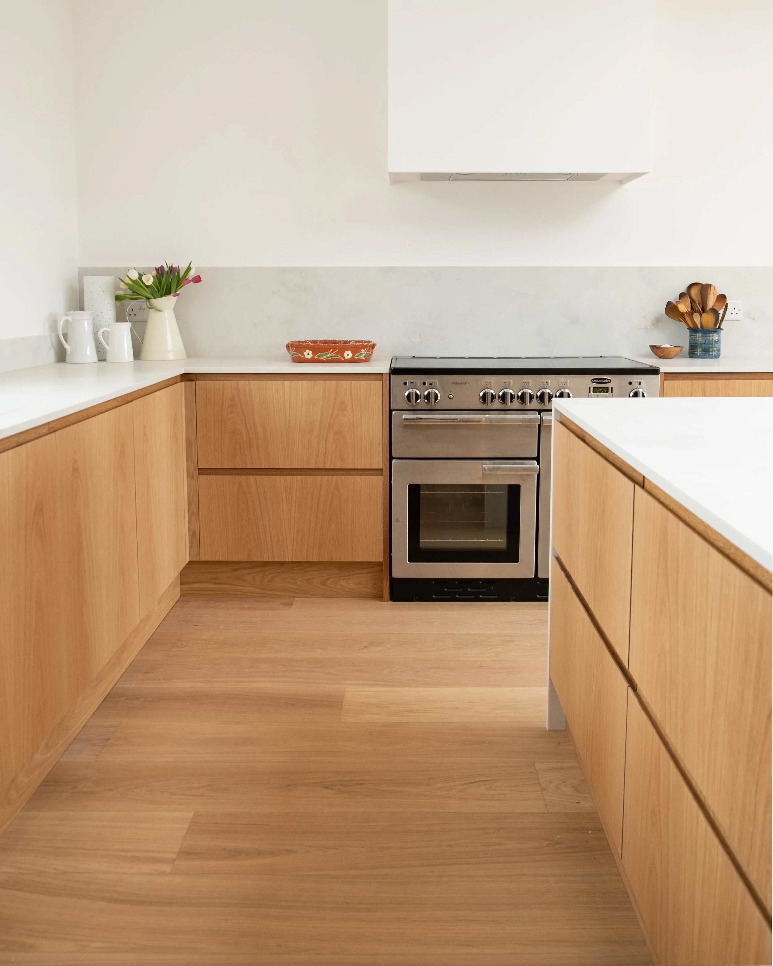 Kitchen with wooden cabinets, a white countertop, a stove, a vase of purple and white tulips, a tea set, a decorative tray, and utensil holders on the counter.