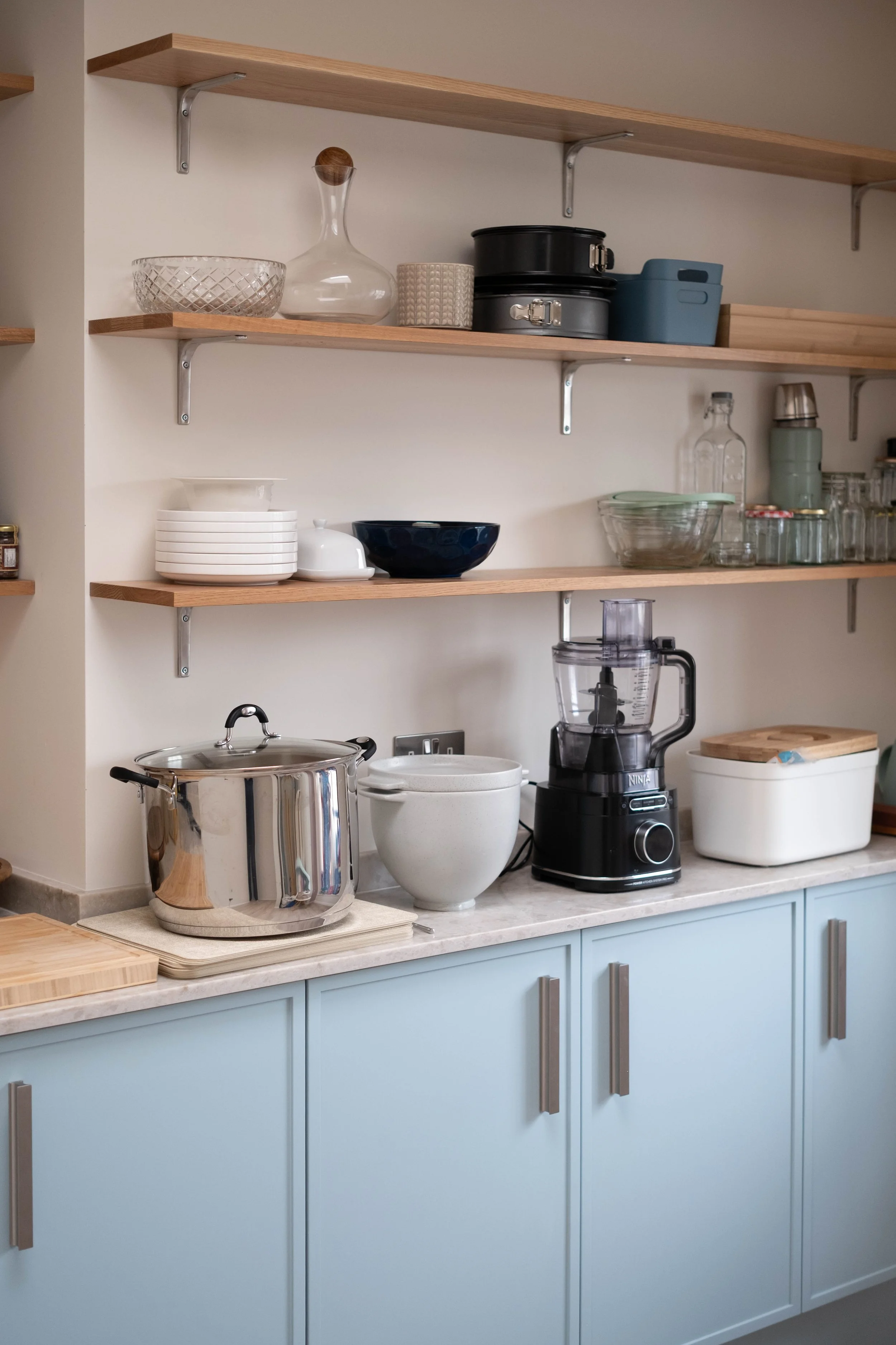 Open kitchen shelves with dishes, bowls, jars, and a blender, with light blue cabinets below.