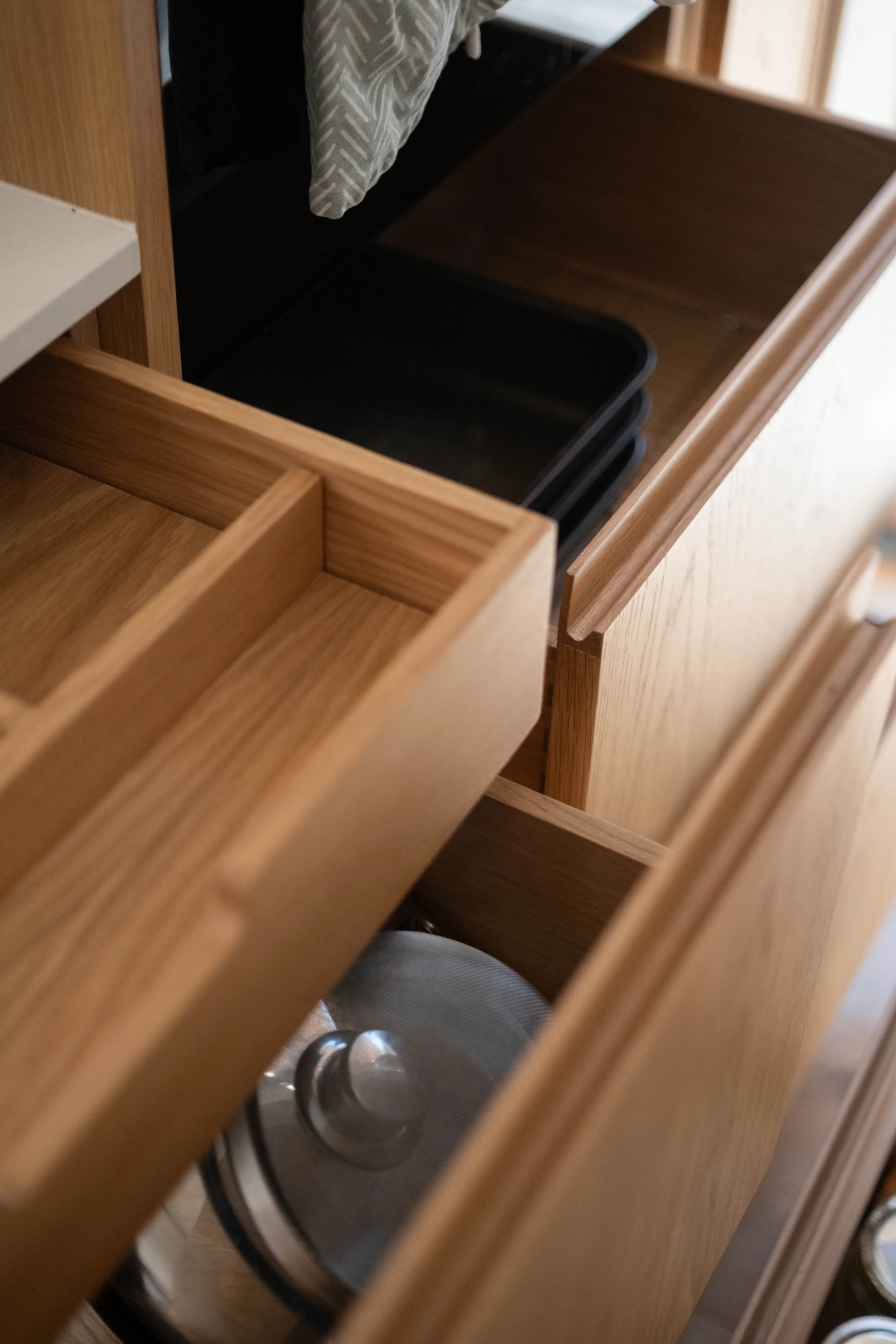 View of a kitchen drawer with black trays, containing pans, seen through the partially open drawer of a wooden cabinet.