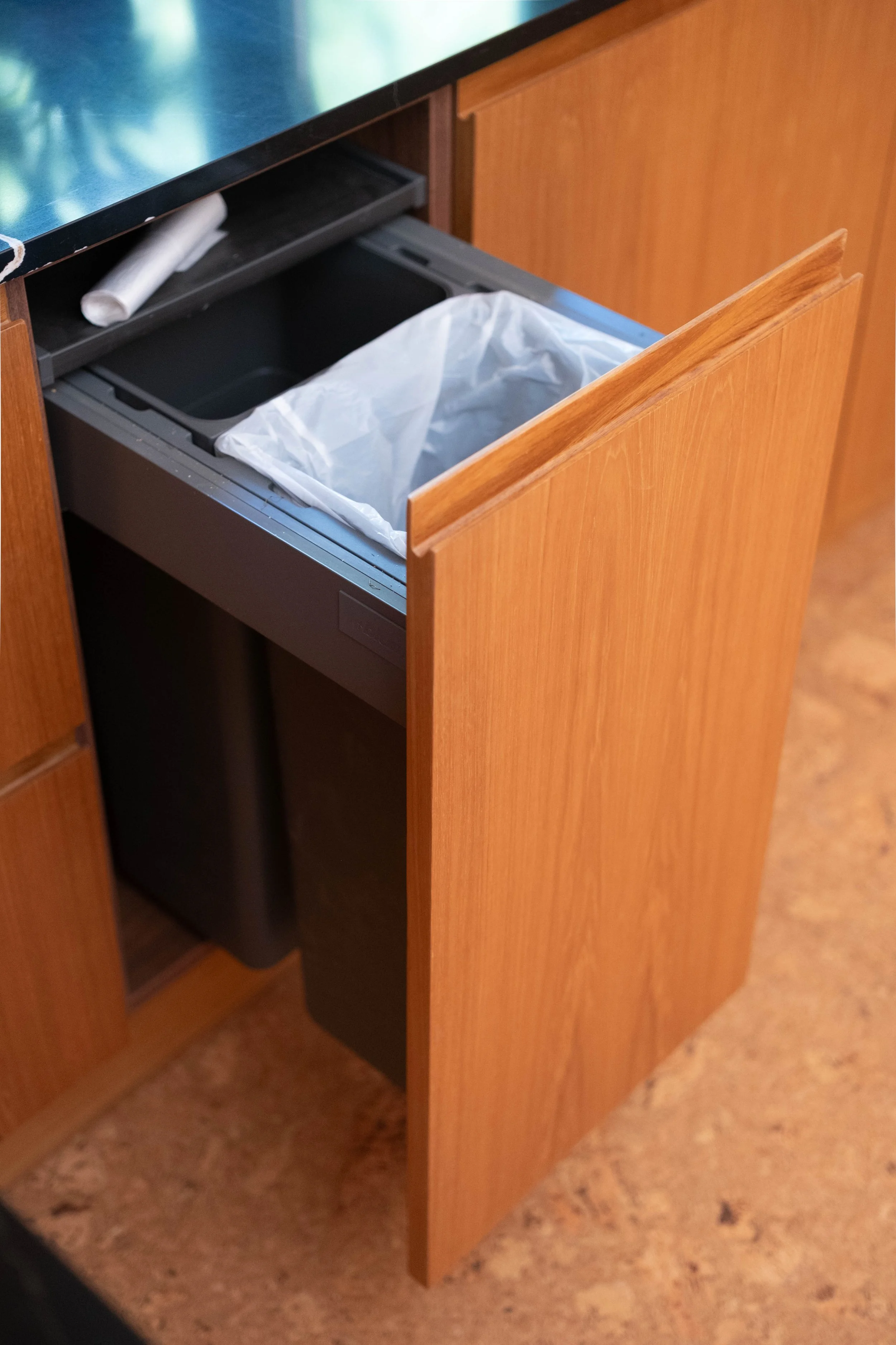 Open wooden cabinet with trash bin inside and a white rolled paper on top shelf.