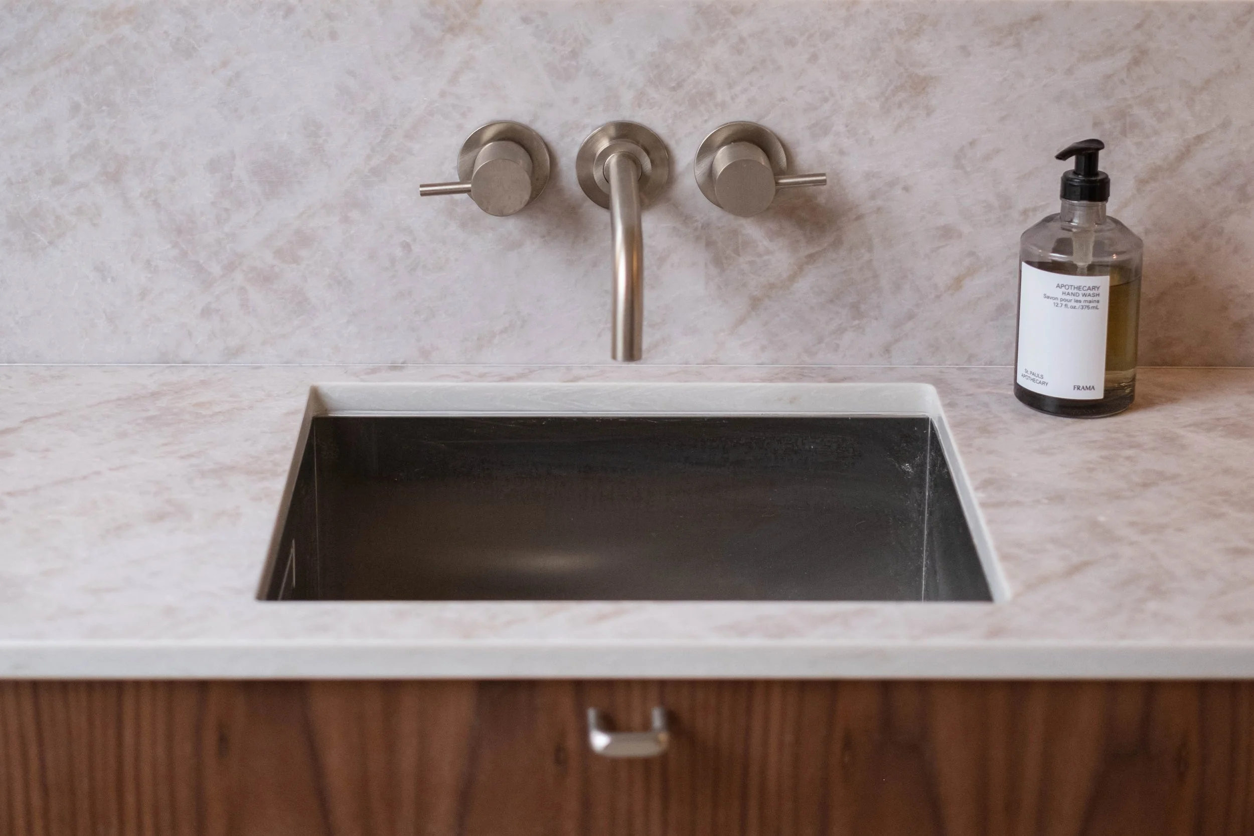 Bathroom sink with a soap dispenser on the right side and a stainless steel faucet above the sink.